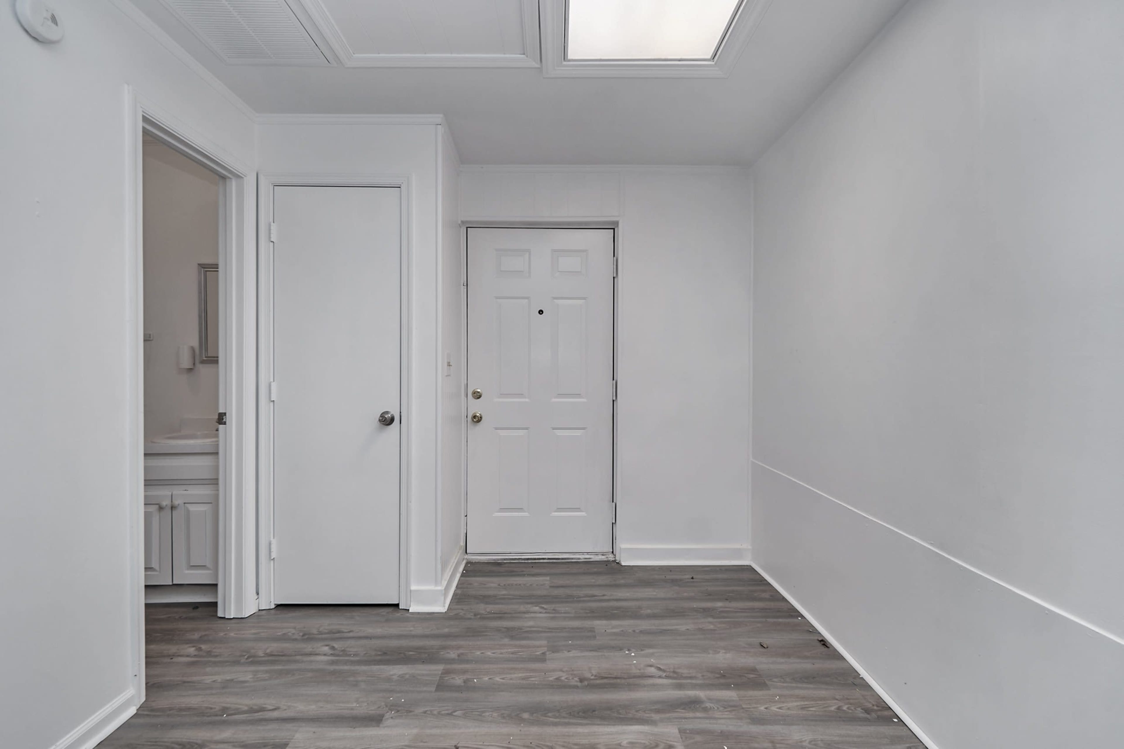A small entryway with a front door and access to a bathroom, featuring white walls and gray laminate flooring.