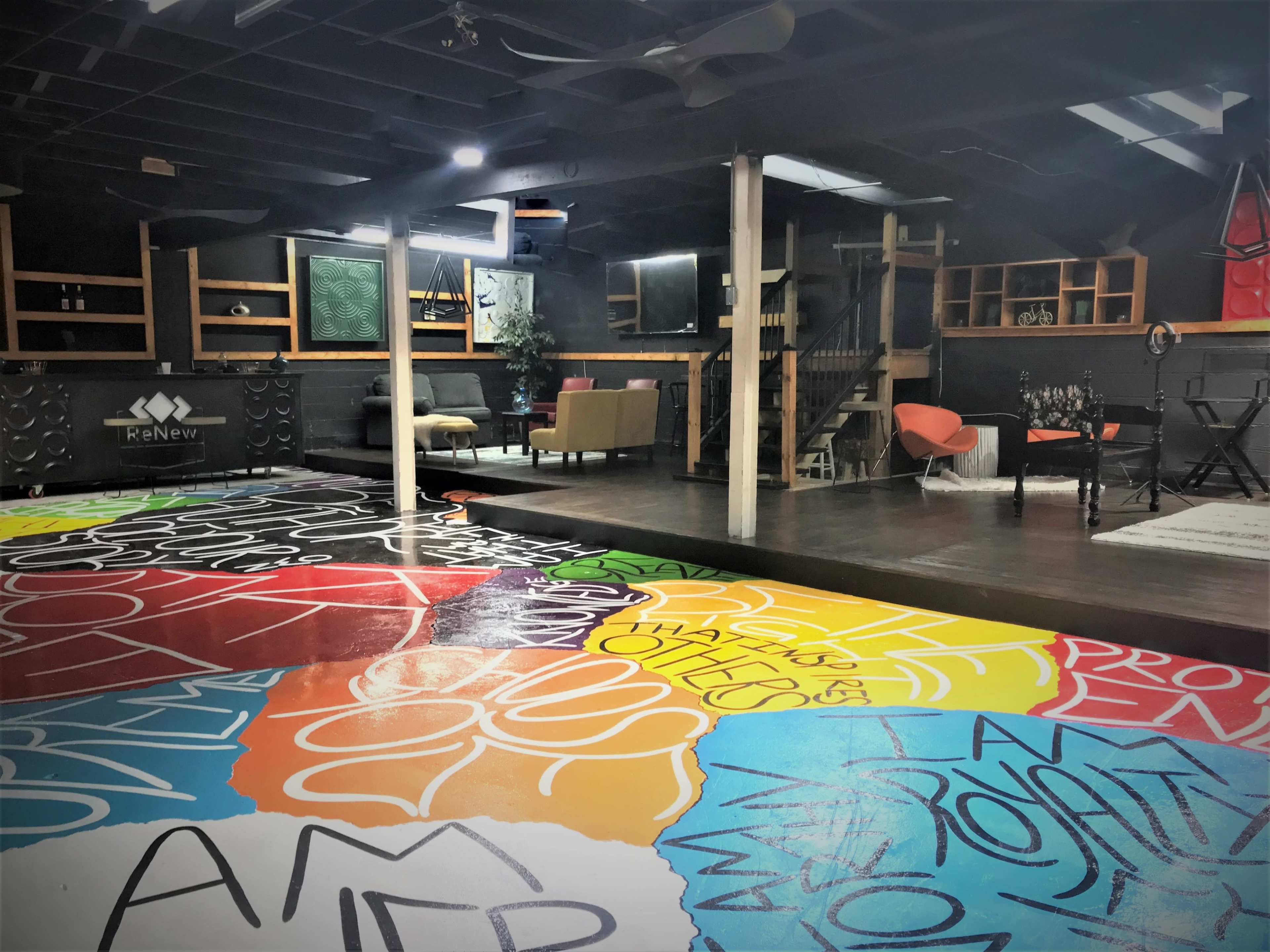A spacious interior with a multicolored graffiti-covered floor, seating areas, and a staircase leading to an upper level.