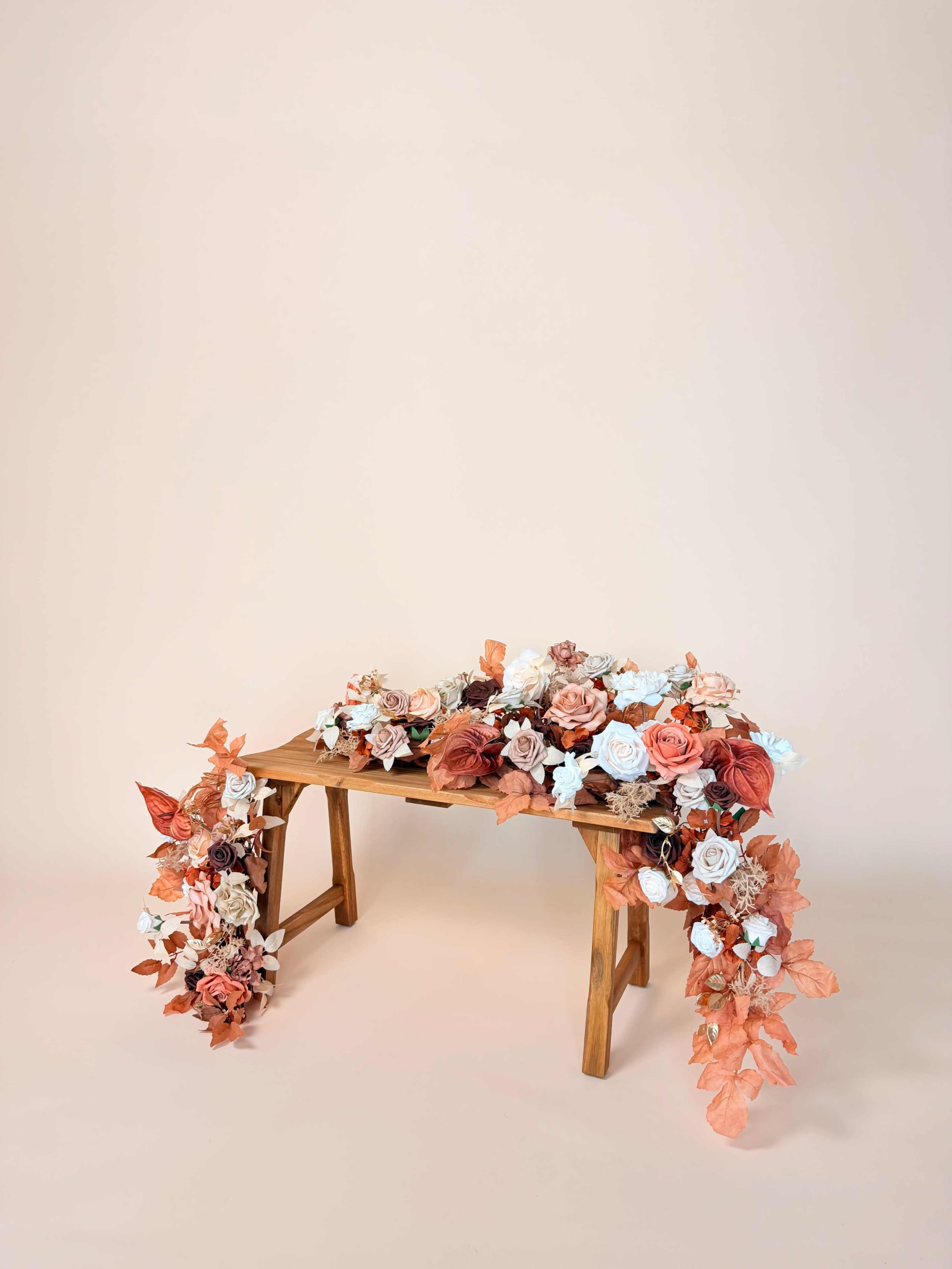 A wooden table is adorned with a floral arrangement of roses and leaves in shades of peach, blue, and red.