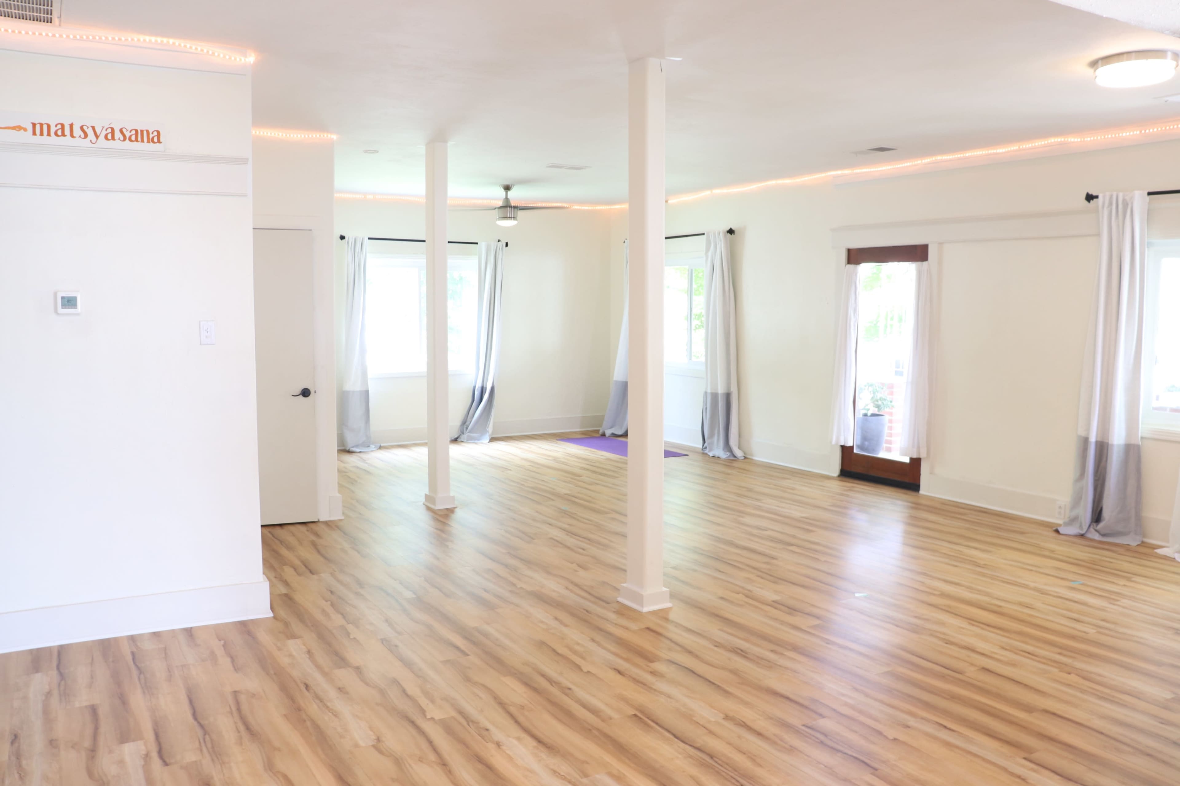 A spacious, well-lit studio with wooden flooring, large windows, and two doors leading outside.