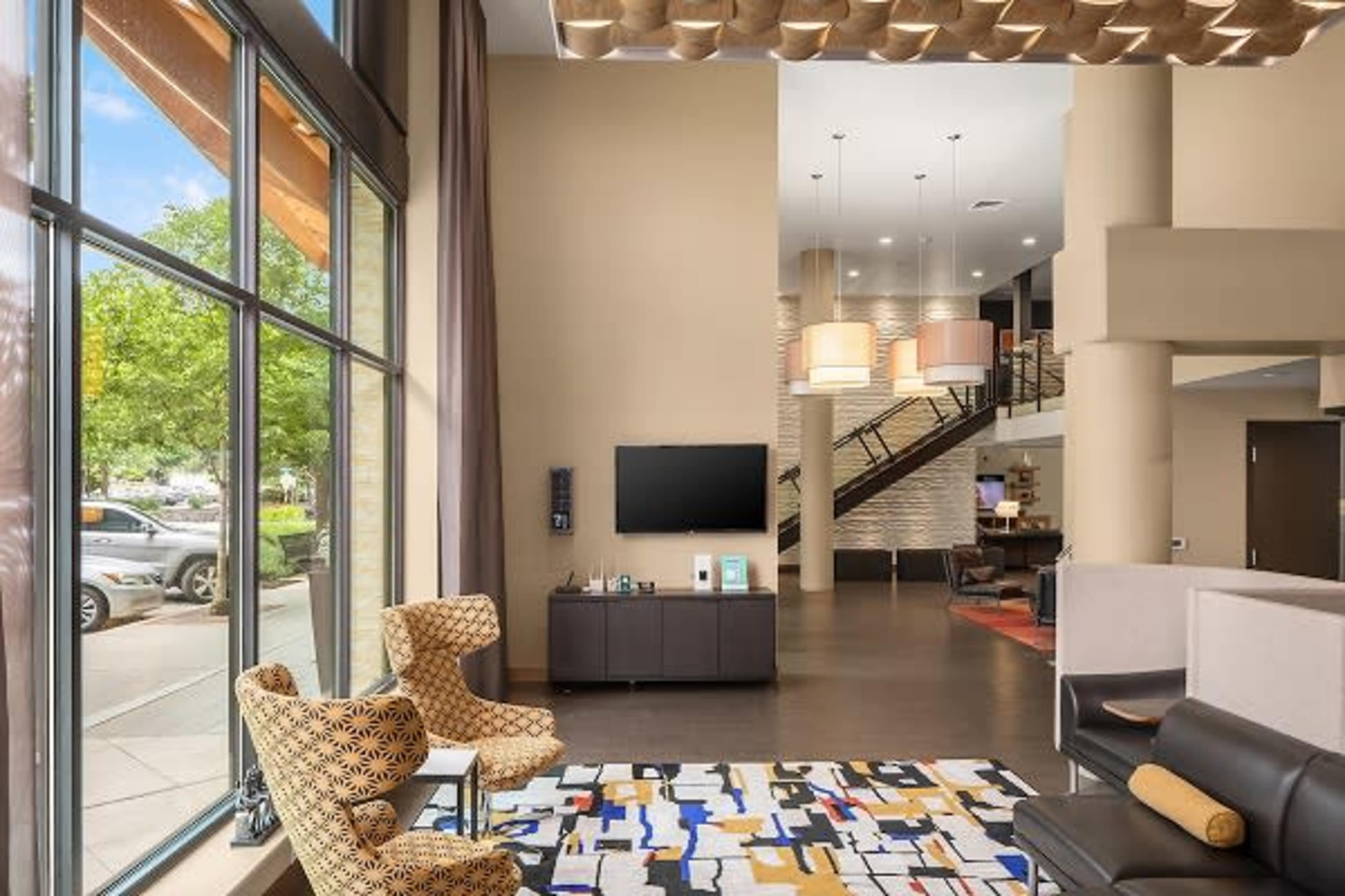 A modern lounge area featuring large windows, a patterned rug, and a staircase leading to an upper level.