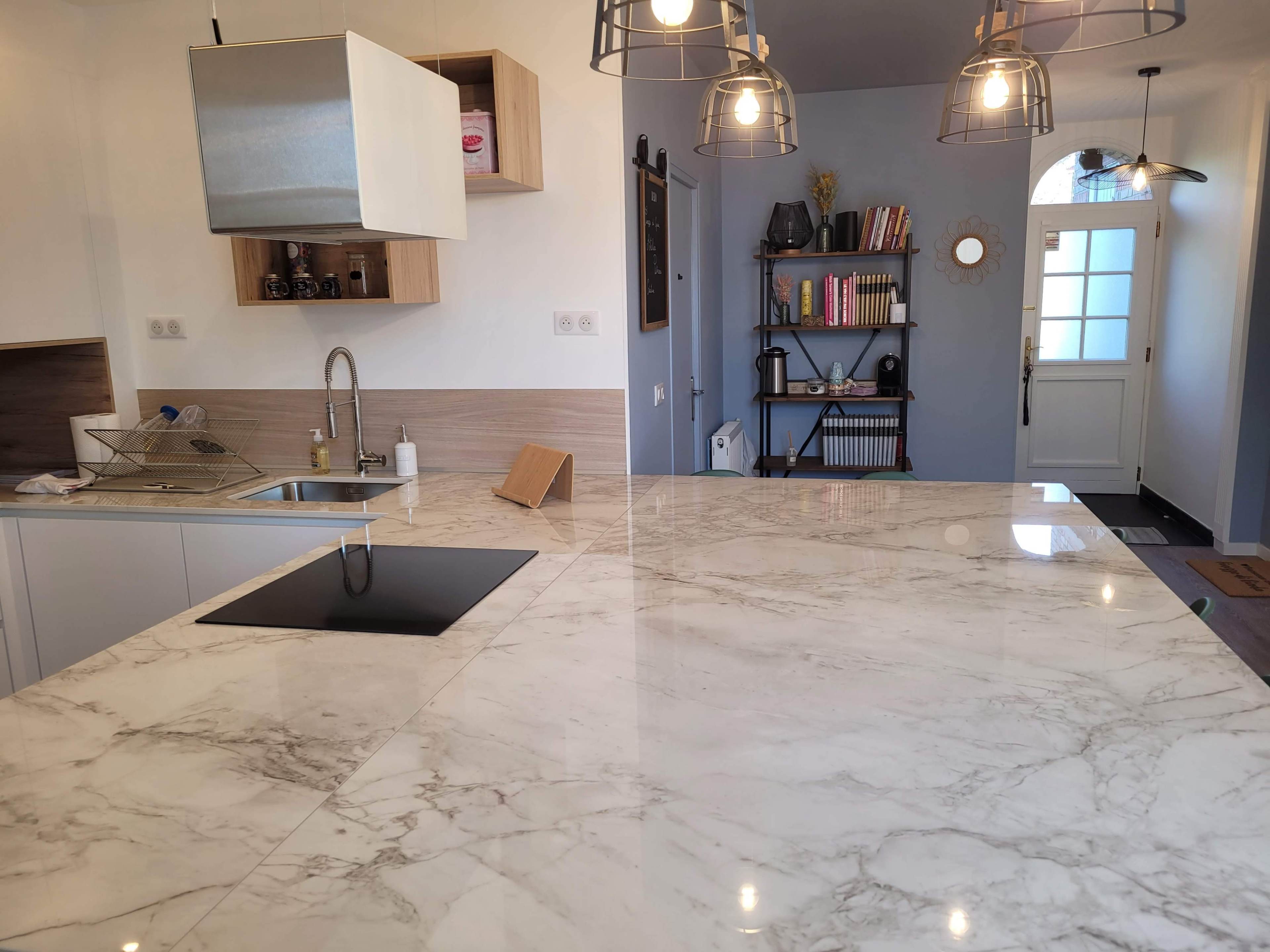 A modern kitchen with a marble countertop, an integrated sink, and a wall-mounted exhaust hood, along with a doorway leading to another room.
