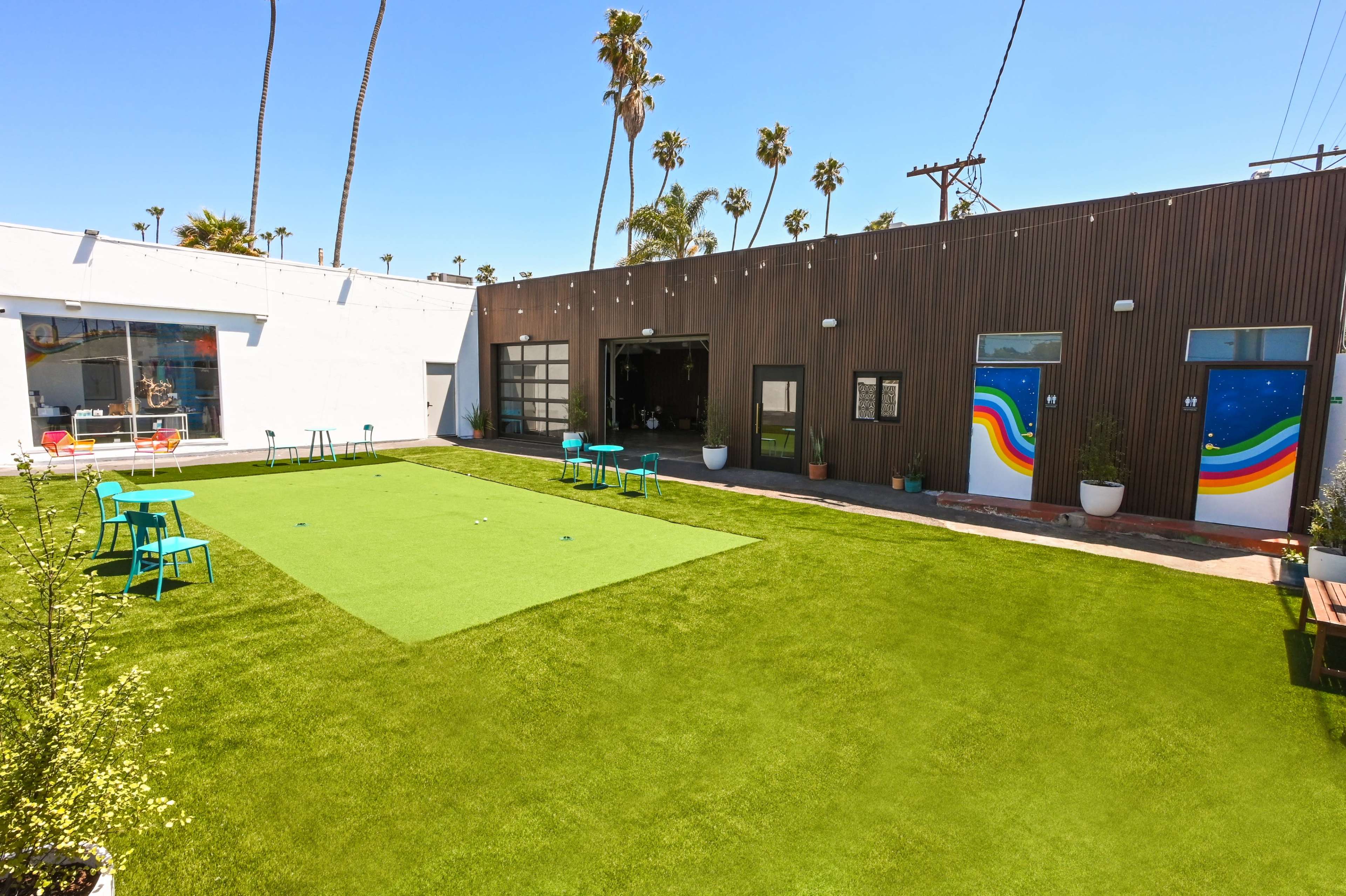 A green, artificial lawn area surrounded by buildings, featuring colorful doors and outdoor seating.