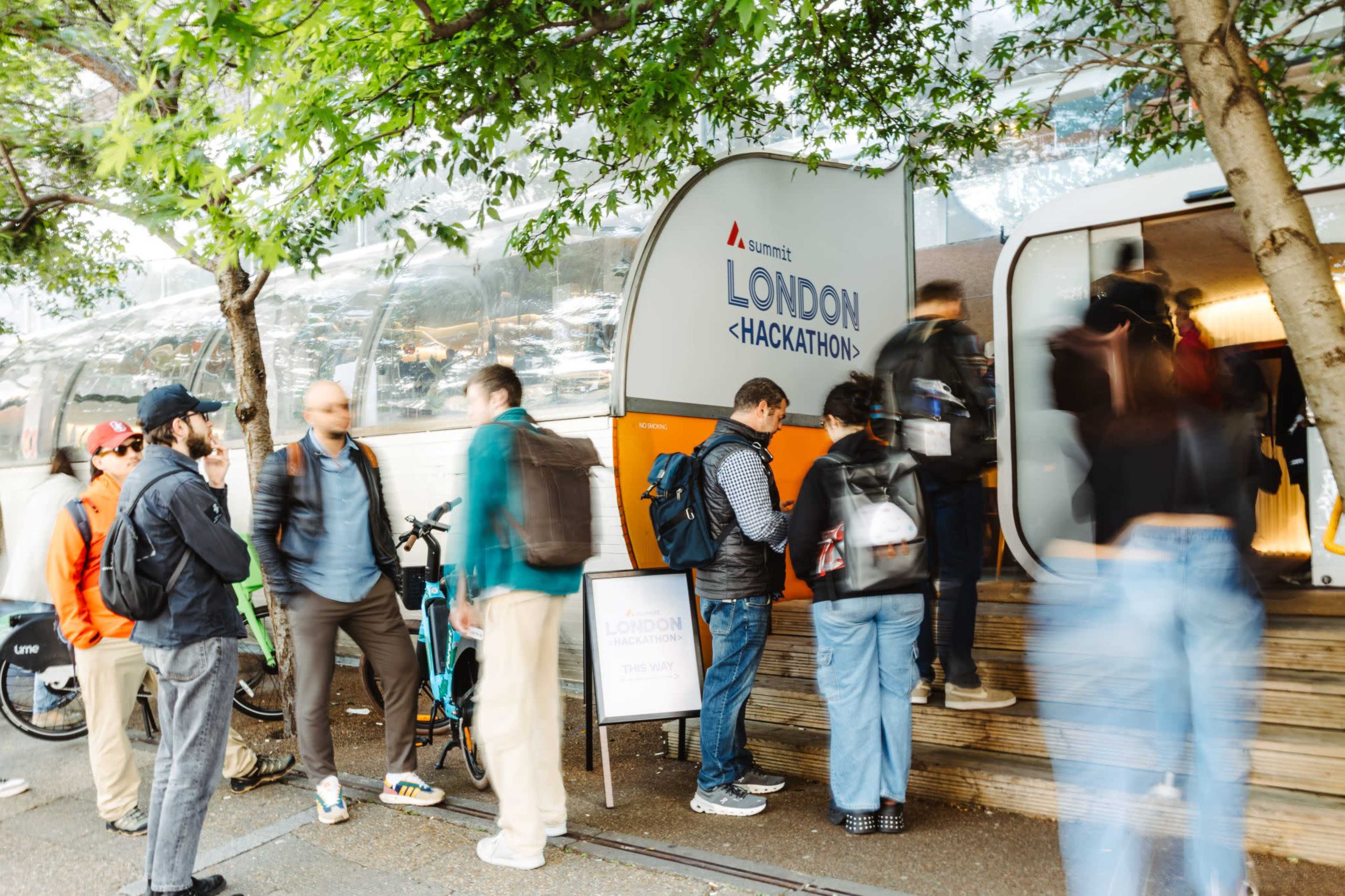 A group of people stands in line outside a building with a sign that reads "LONDON <HACKATHON>."
