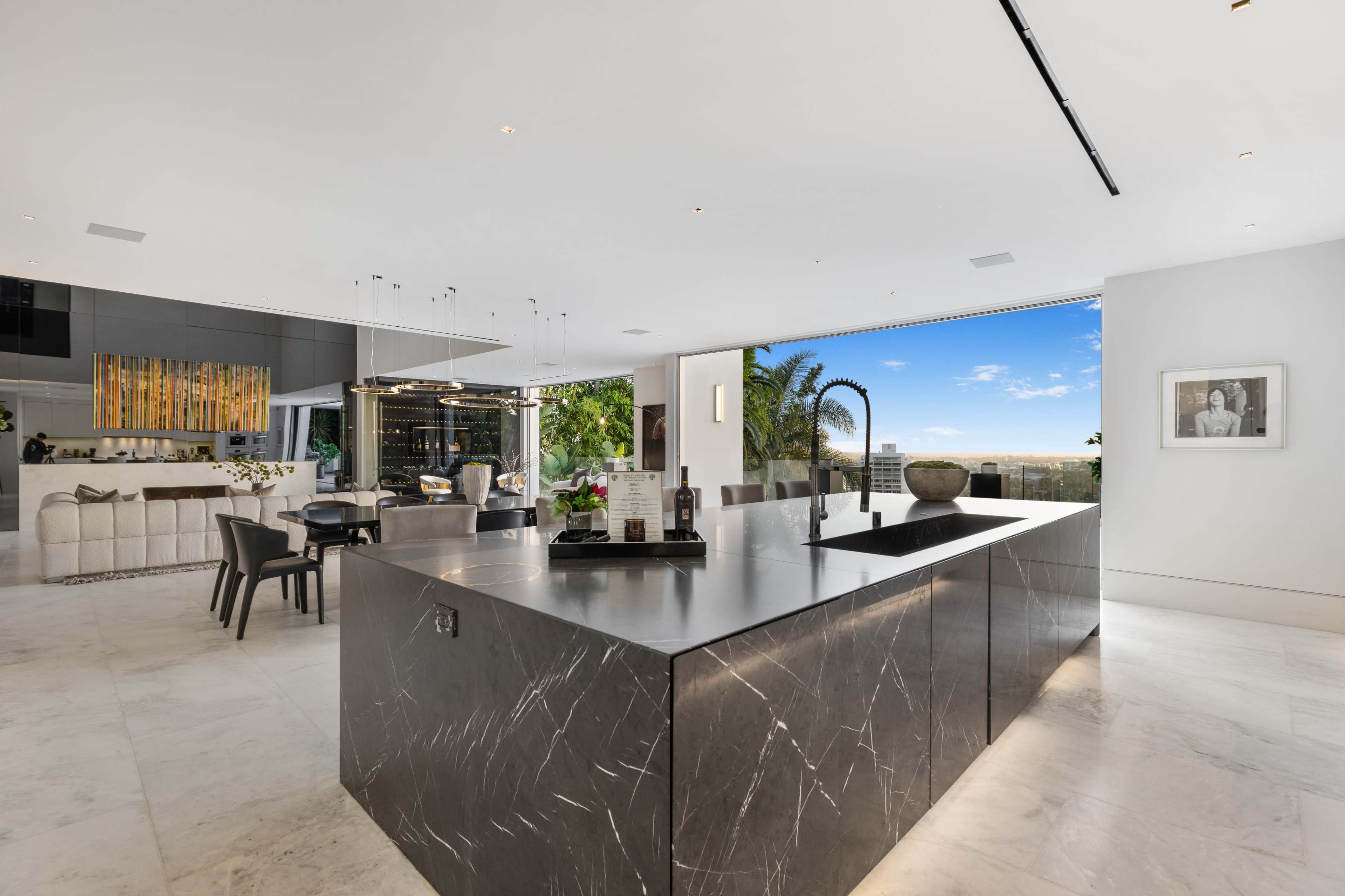 The image shows a modern, open-concept kitchen and dining area with marble flooring and a large island in the center.
