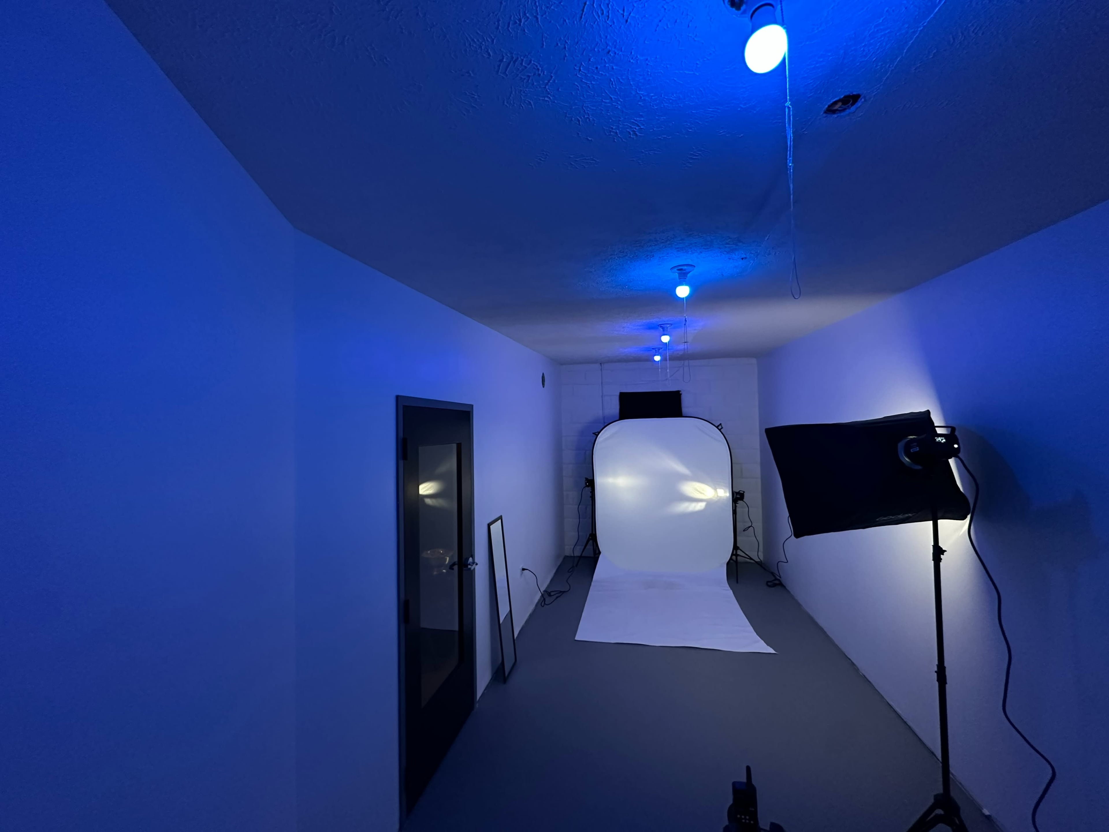 A photography studio with blue lighting, a white backdrop, and a light stand set up in an empty space.