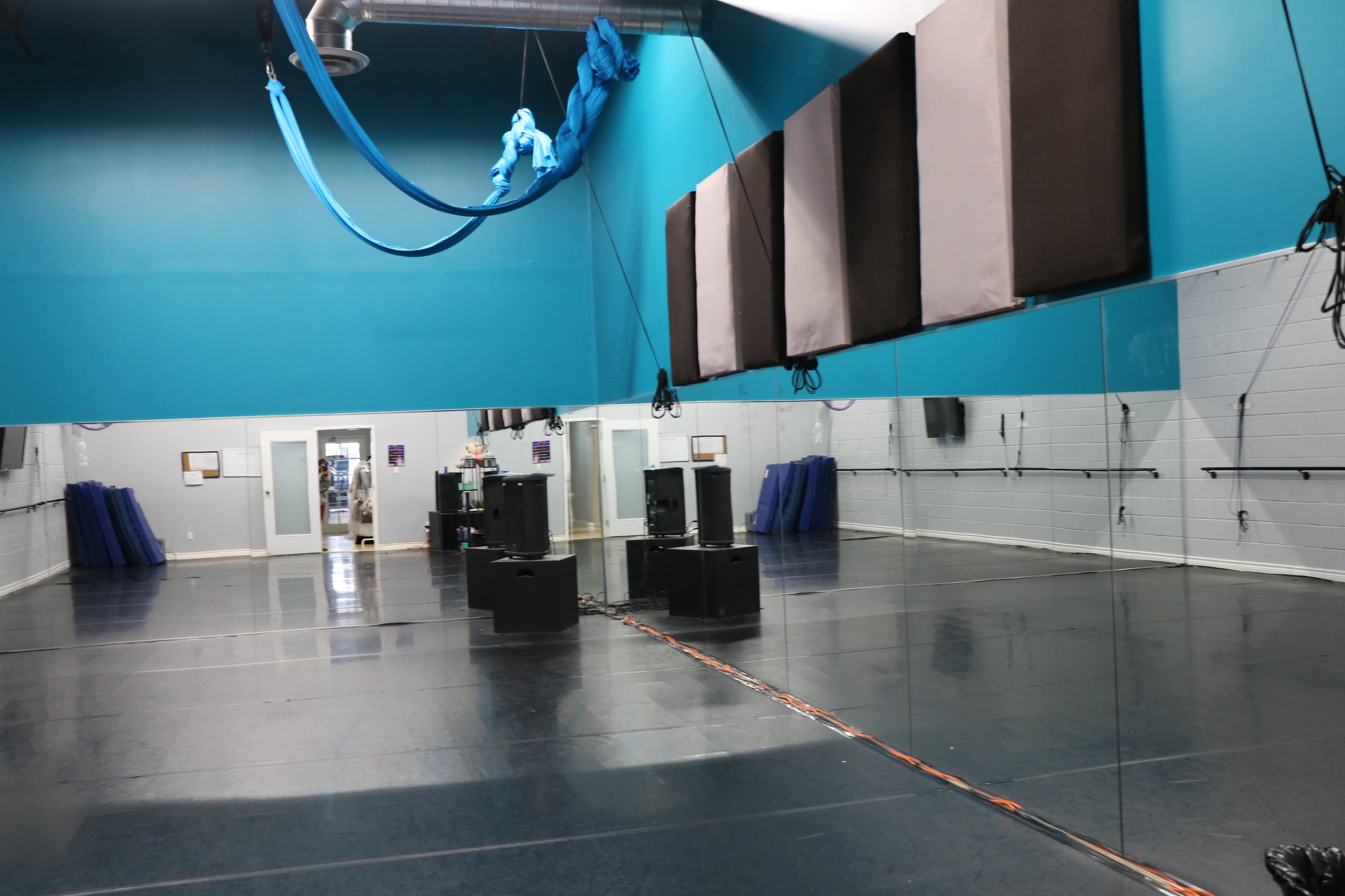 A spacious dance studio features a mirrored wall, black flooring, and aerial silks hanging from the ceiling.