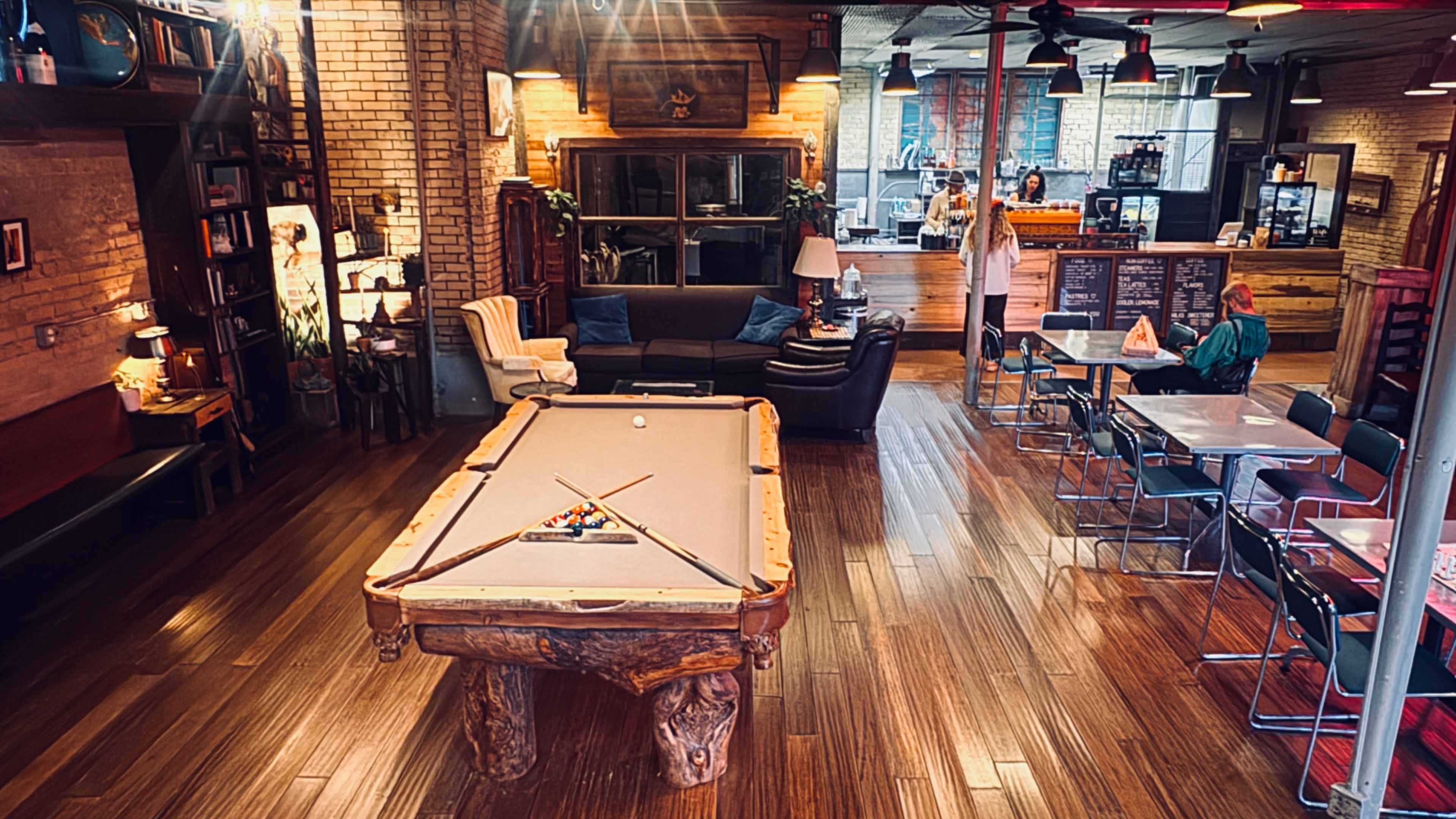 The image shows a spacious, well-decorated interior with a pool table in the center, surrounded by seating areas and wooden floors.