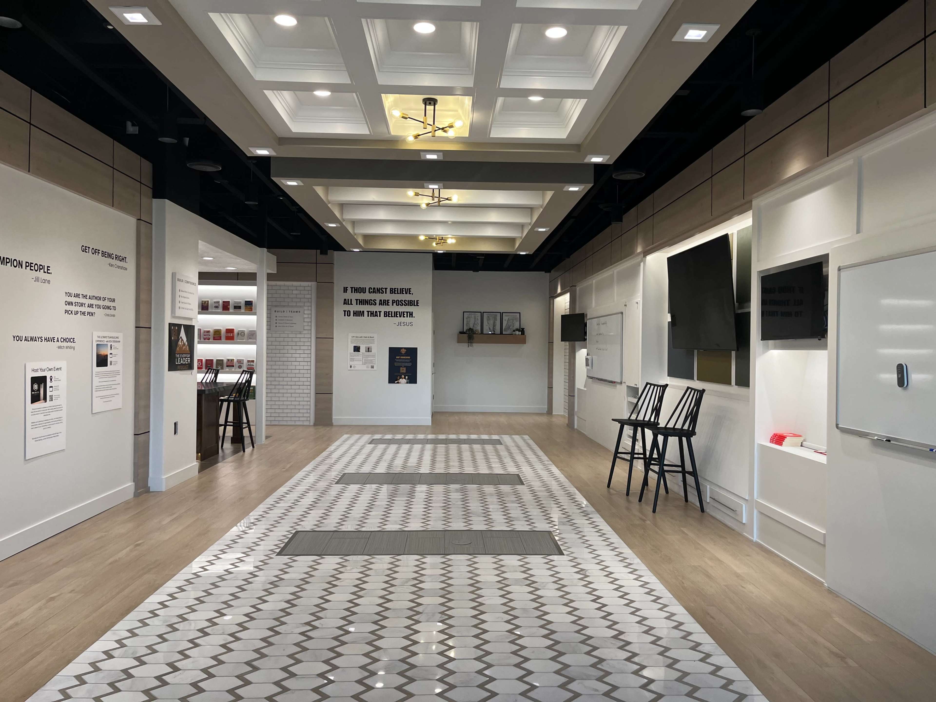 The image shows a modern, well-lit interior space with a tiled floor, featuring seating areas, walls with informational displays, and a symmetrical layout.
