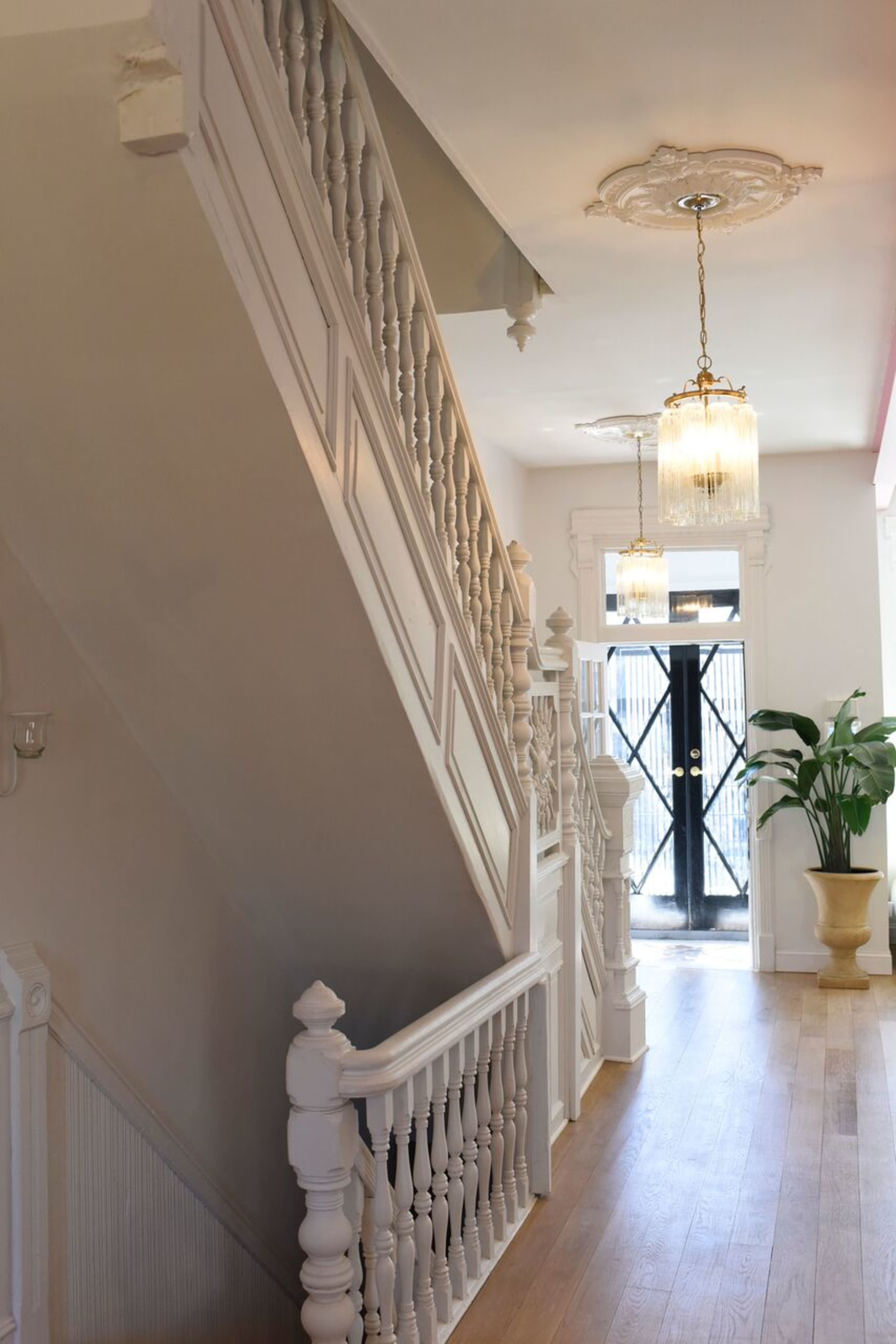 A well-lit staircase with white banisters and a decorative ceiling fixture, leading to a door with glass panels.