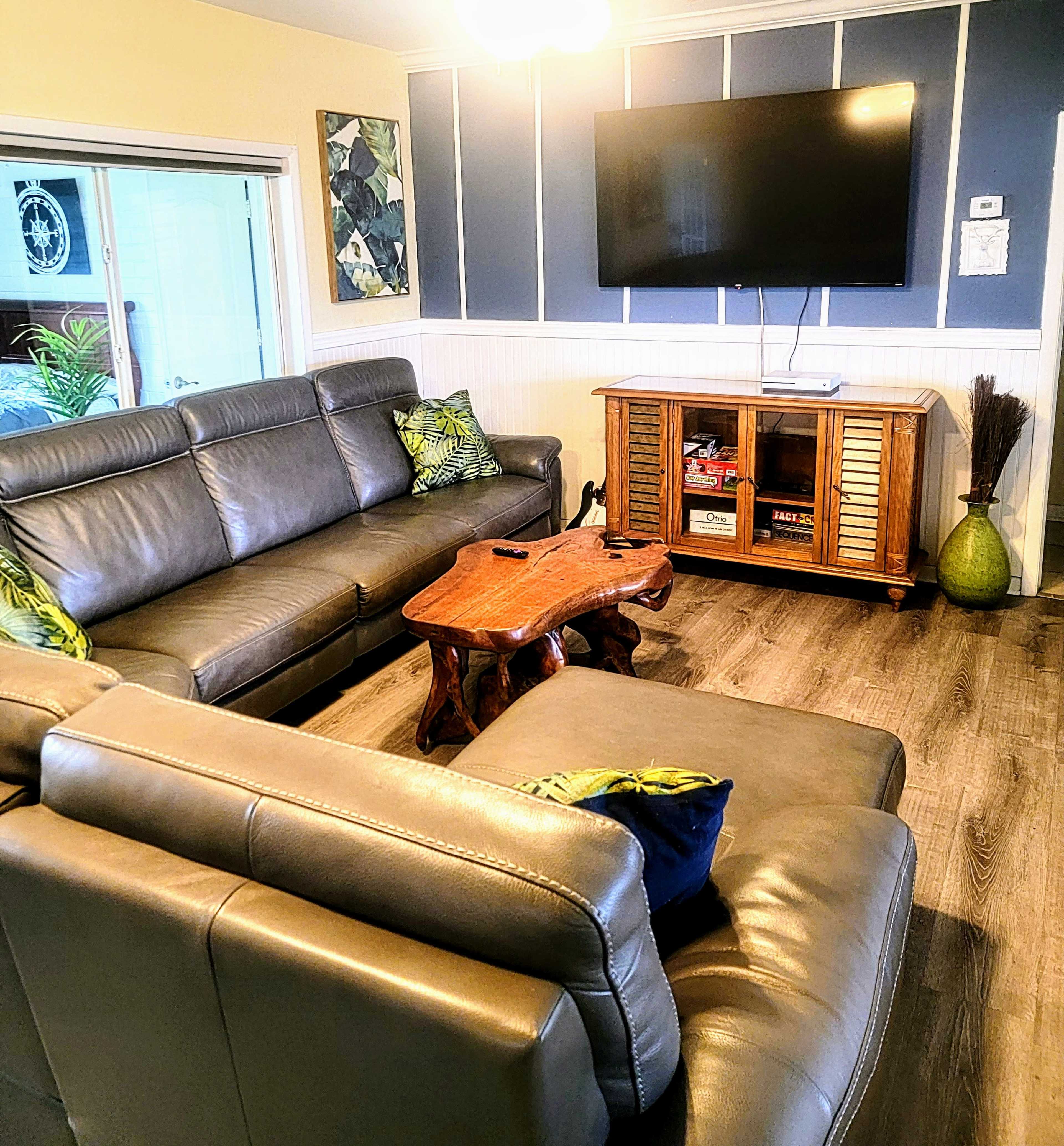 A living room with gray leather couches, a wooden coffee table, and a wall-mounted television above a wooden cabinet.