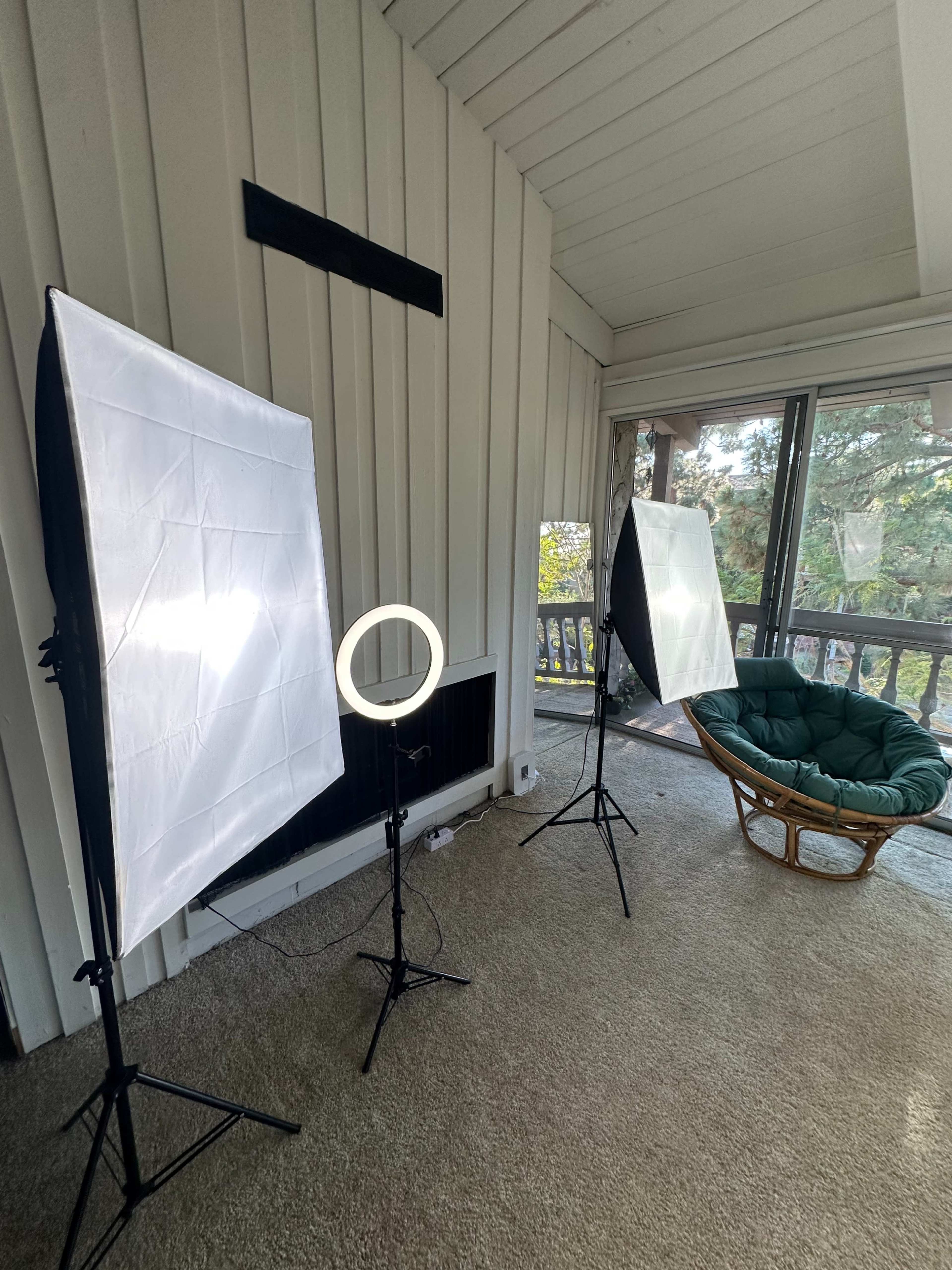 The image shows a well-lit room with two softbox lights and a ring light set up around a green cushioned chair.