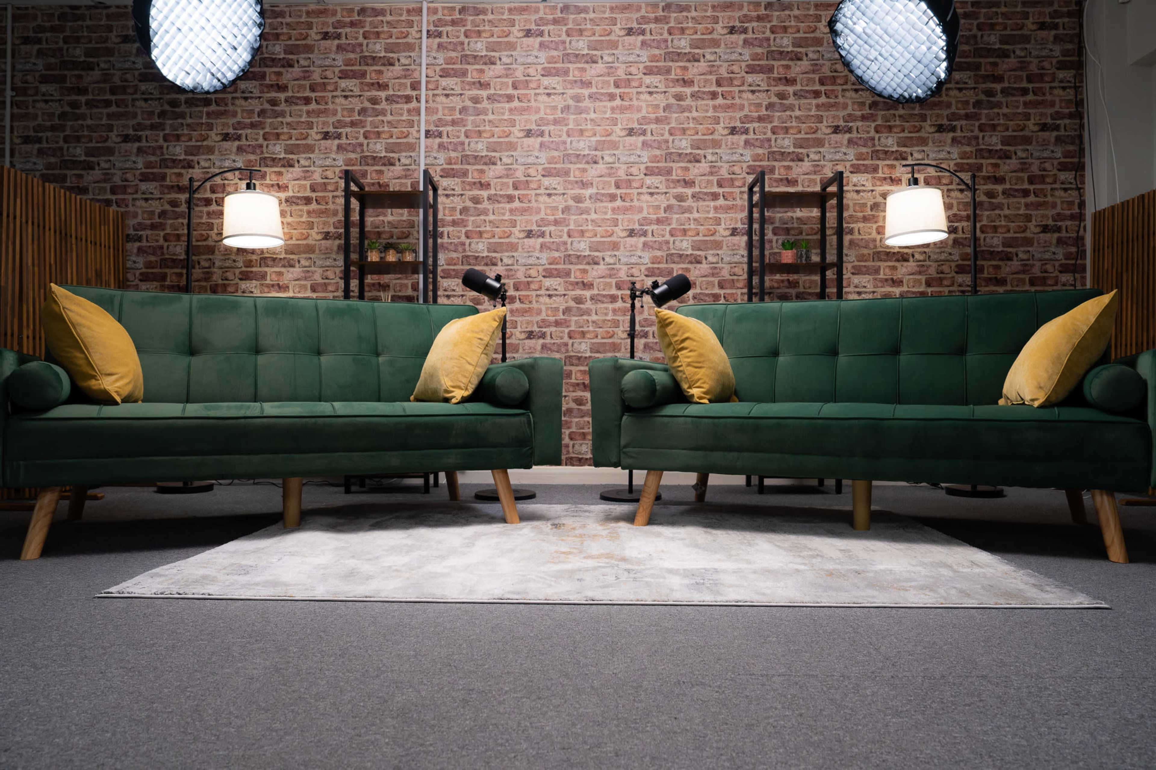 The image shows two green sofas with yellow pillows facing each other in a room featuring a brick wall and lighting fixtures.