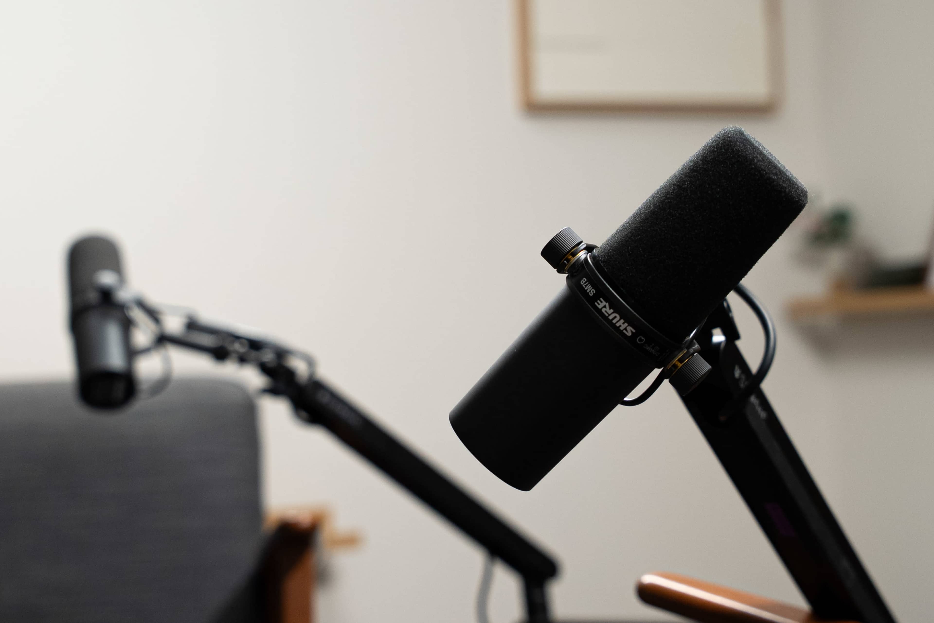 Two microphones are positioned on adjustable arms in a minimalist recording studio setting.