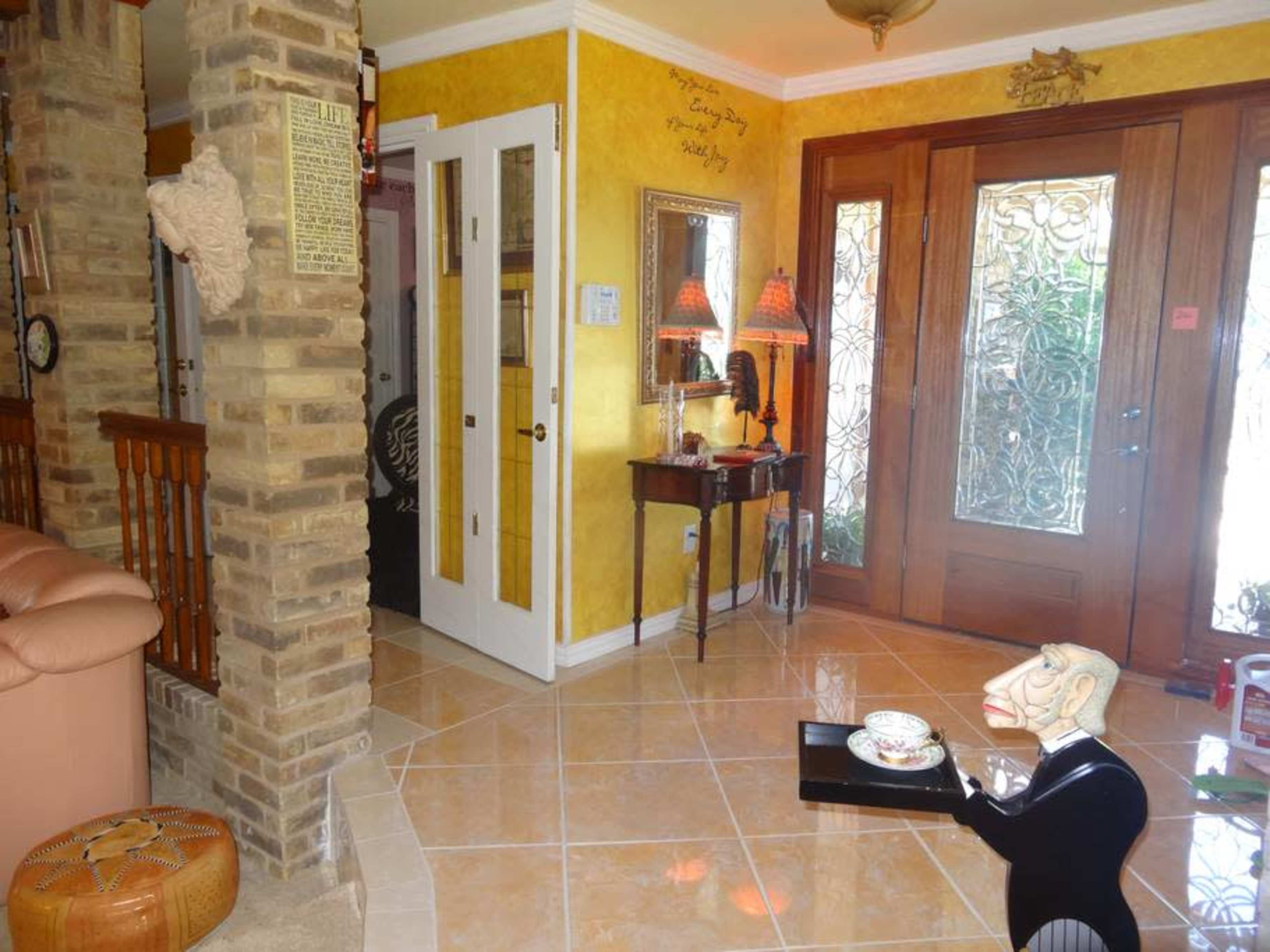 A well-decorated foyer with yellow walls, elegant double doors, and various decorative elements, including a unique figurine and stylish lighting.