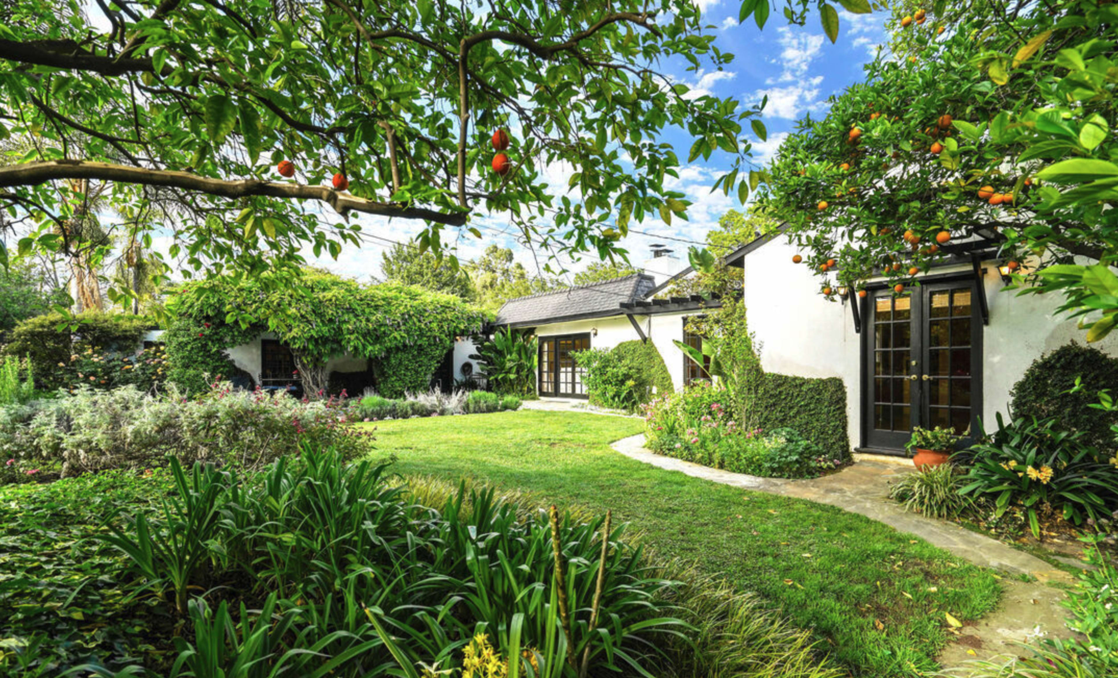 A quaint house is surrounded by a lush garden filled with greenery and fruit-bearing trees.