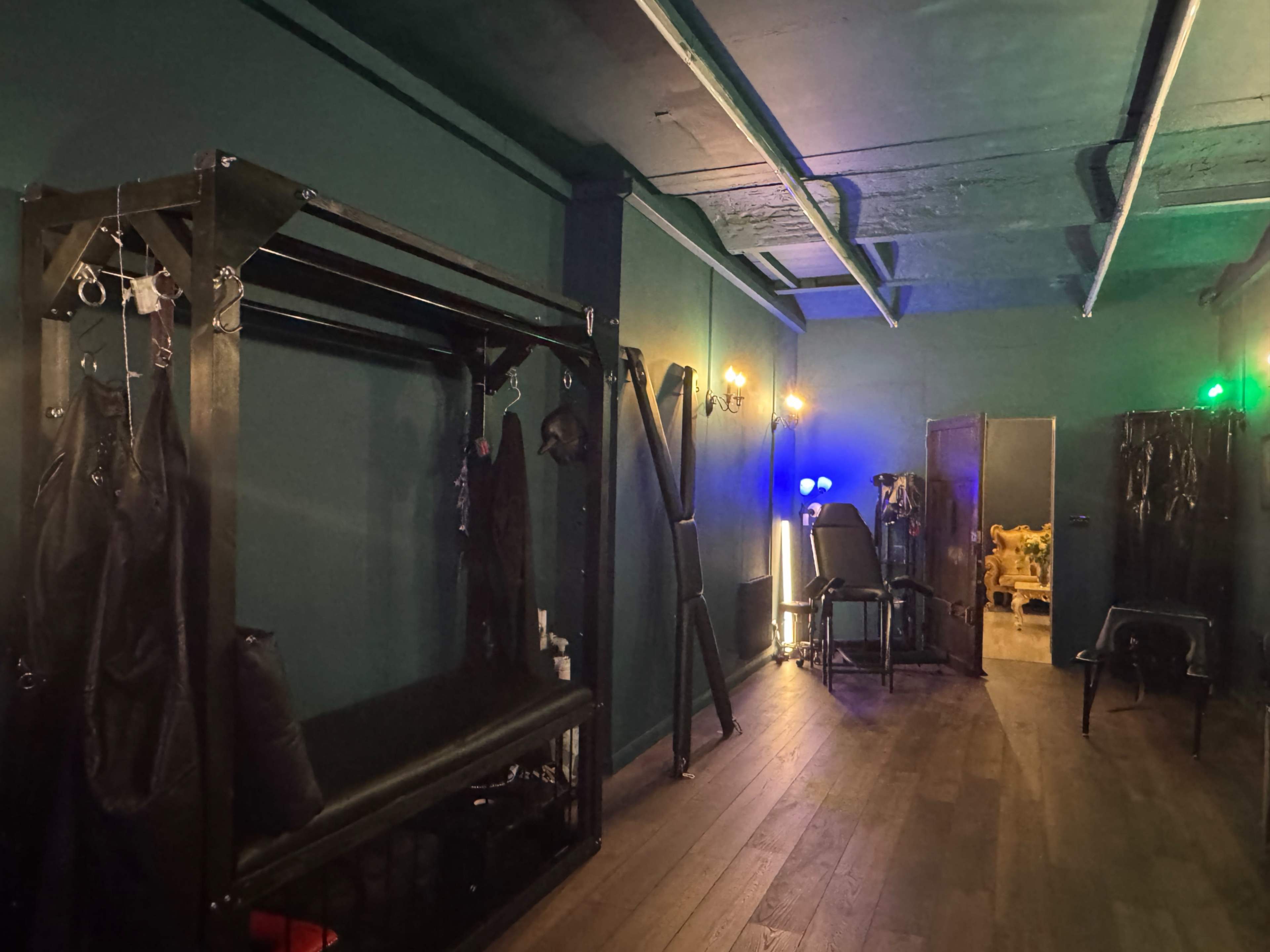 The image shows a dimly lit room with dark green walls, featuring metal racks on one side and various chairs scattered throughout.