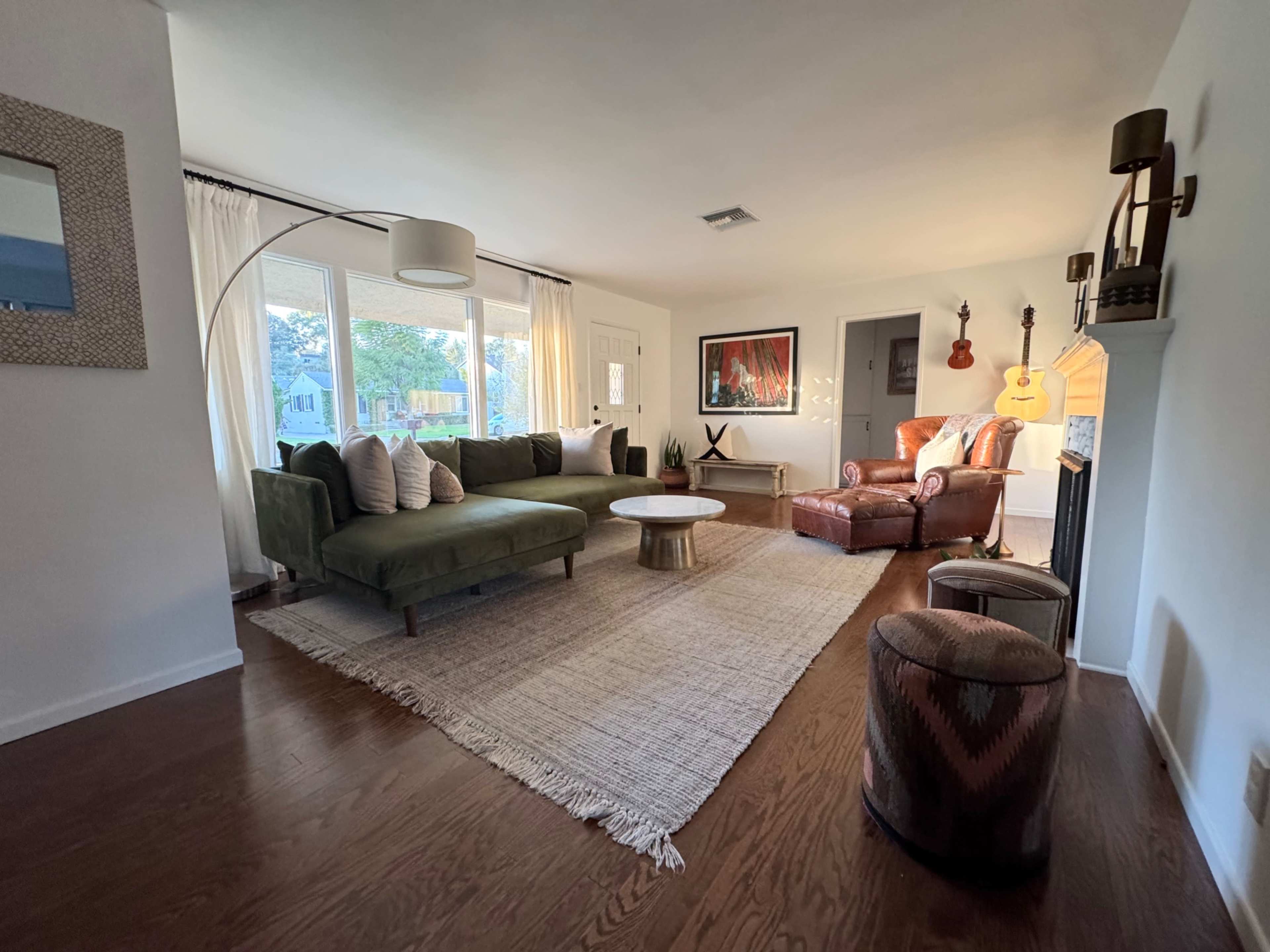 The image shows a well-lit living room featuring a green sectional sofa, a round coffee table, and a mix of decorative furniture, including an armchair and a pouf.
