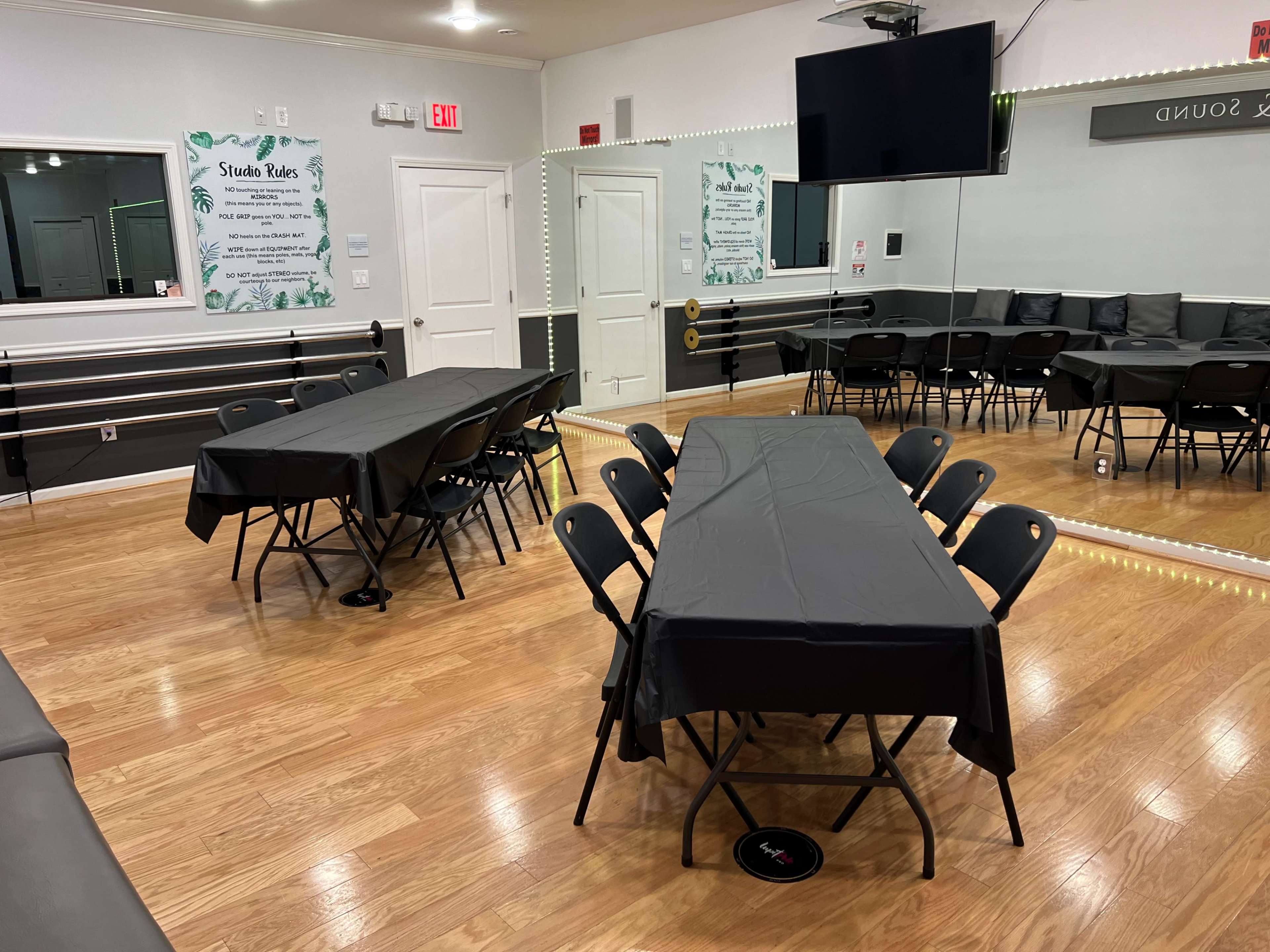 The room features several black foldable tables covered with black tablecloths, arranged in a spacious area with chairs set around them and mirrors along the walls.