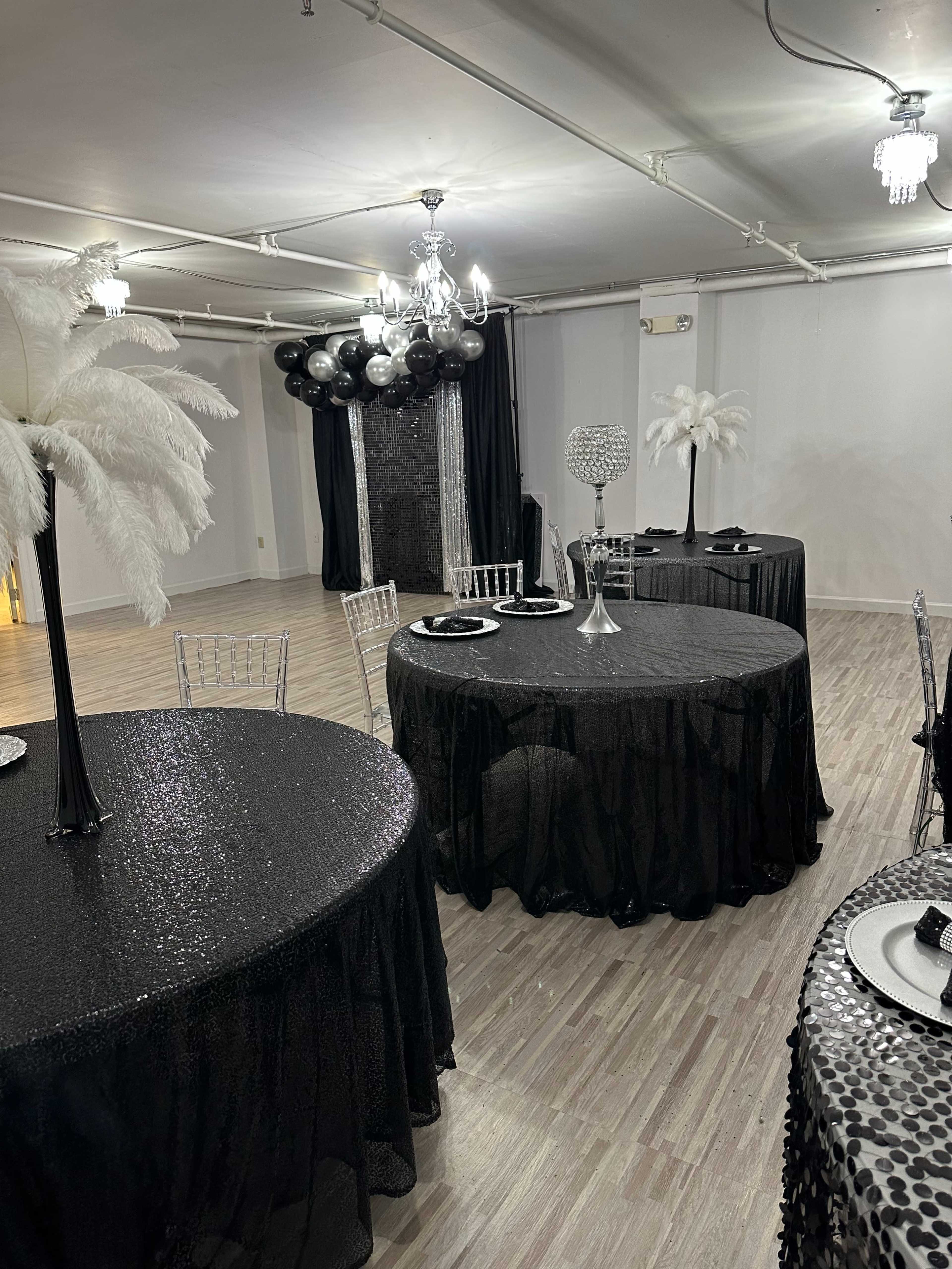 A banquet hall decorated with black and white tables, featuring feather centerpieces and elegant tableware.