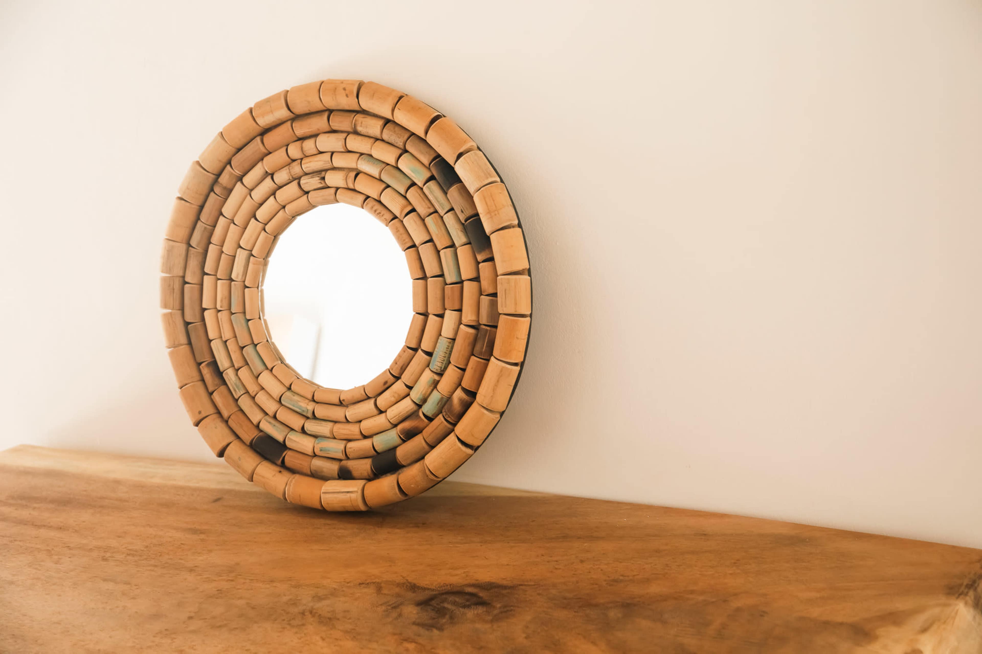 A round mirror with a wooden cork frame is positioned on a wooden surface against a plain wall.