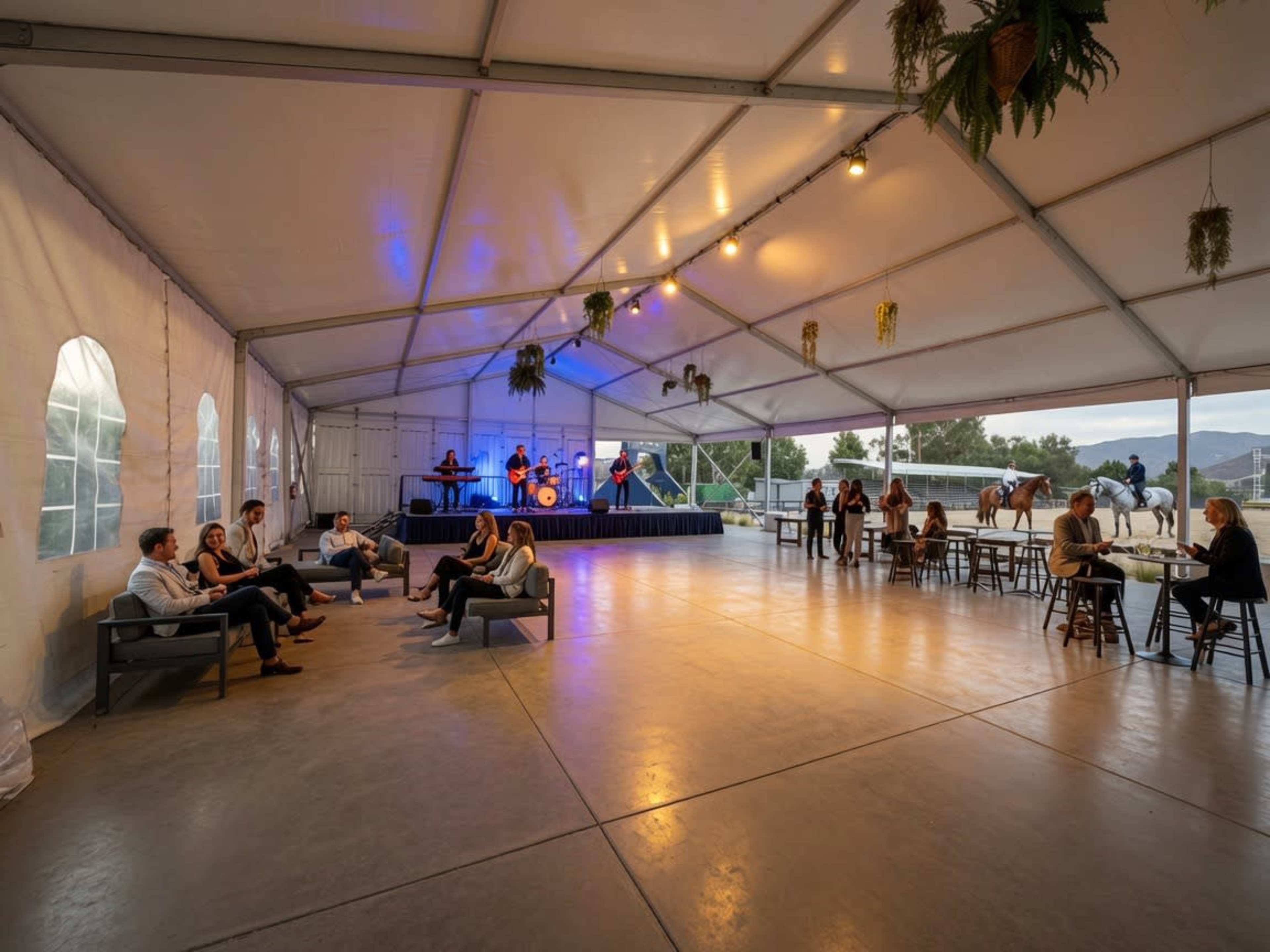 A large, covered tent features a band playing on stage while guests socialize and enjoy the space.