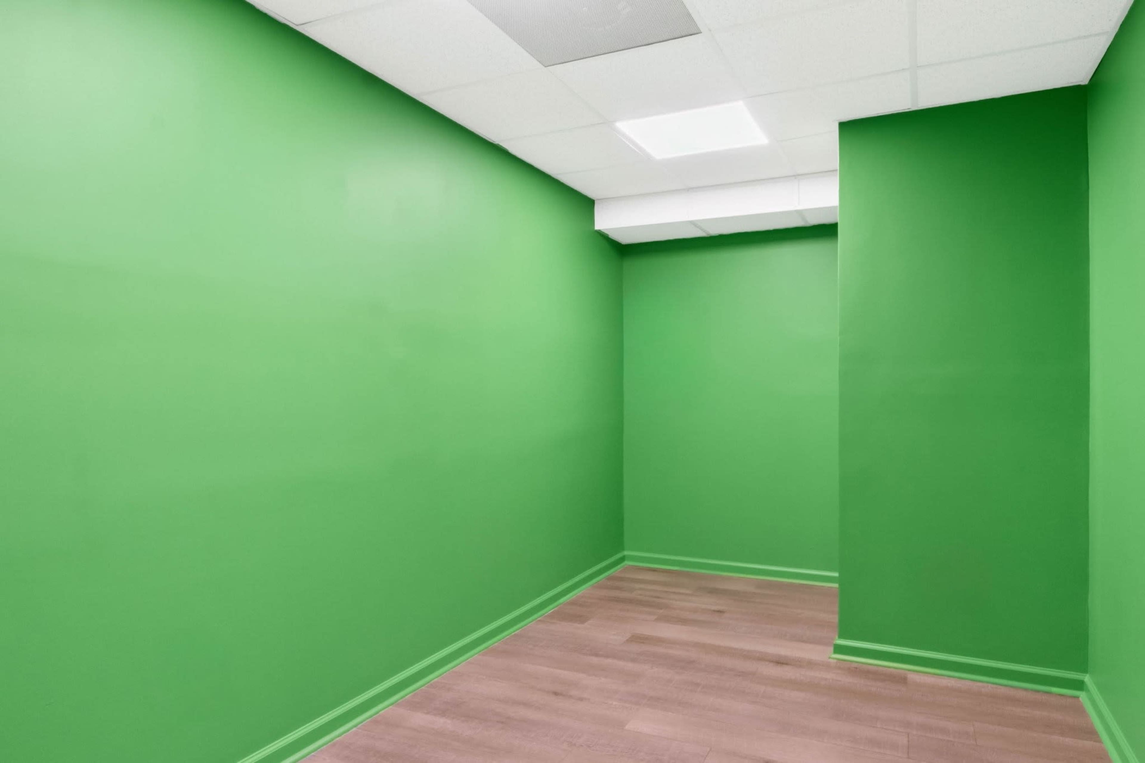 The image shows a small empty room with bright green walls and a wooden floor.