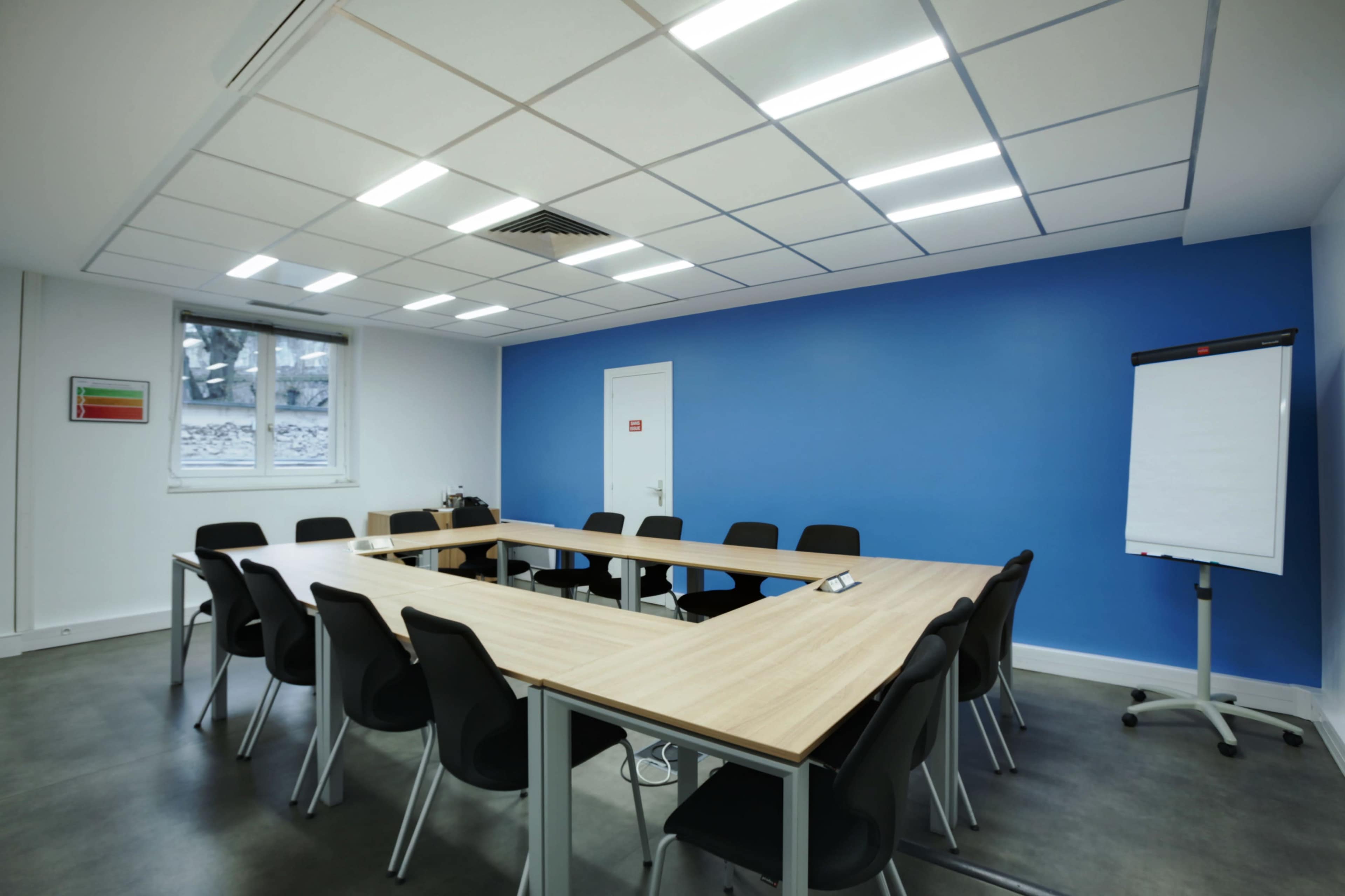 A conference room with a large, oval table surrounded by black chairs and a blue accent wall.
