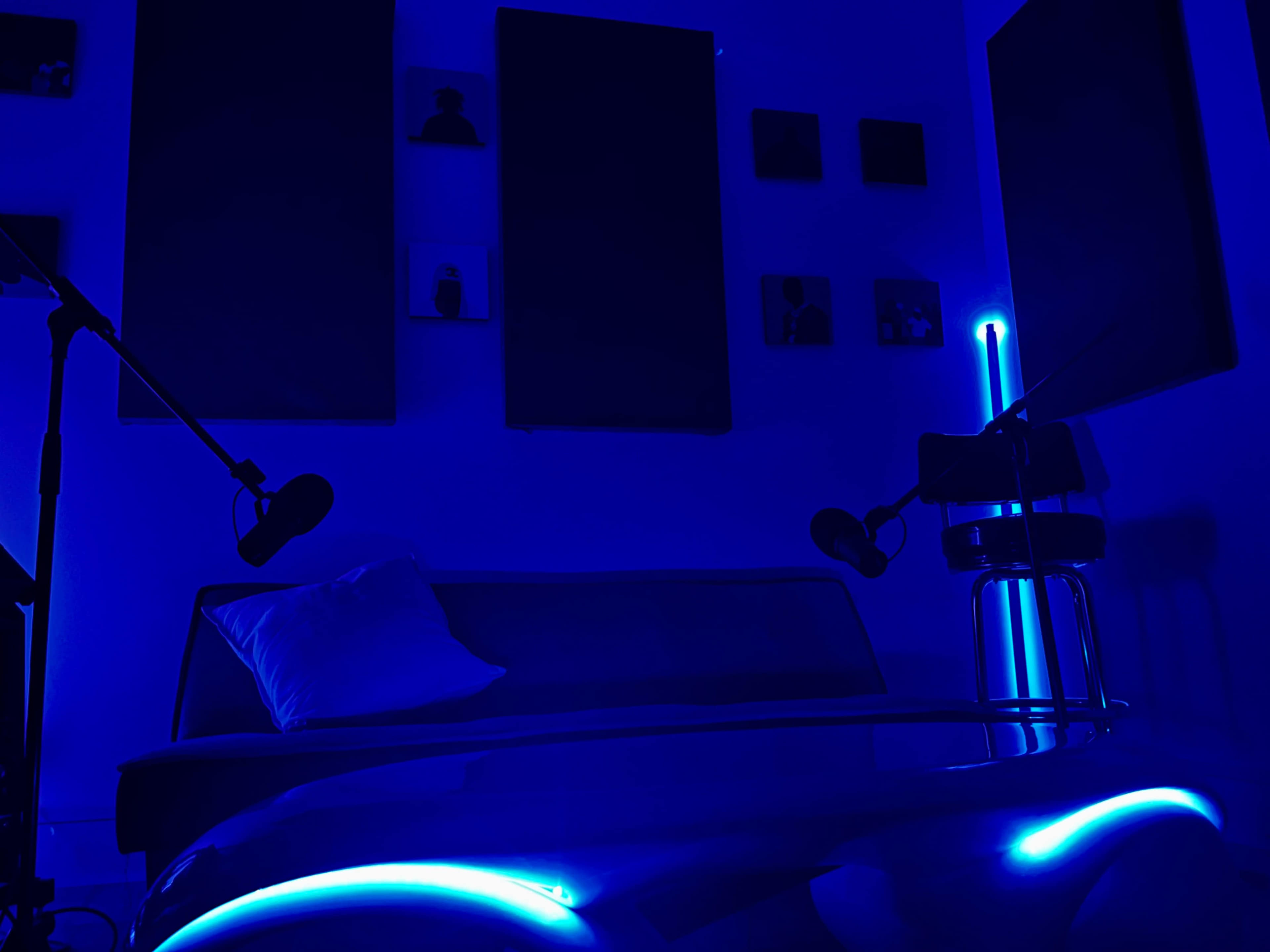 A dimly lit room with a blue hue features a sofa, a glass table with blue lighting, and two microphones on stands.