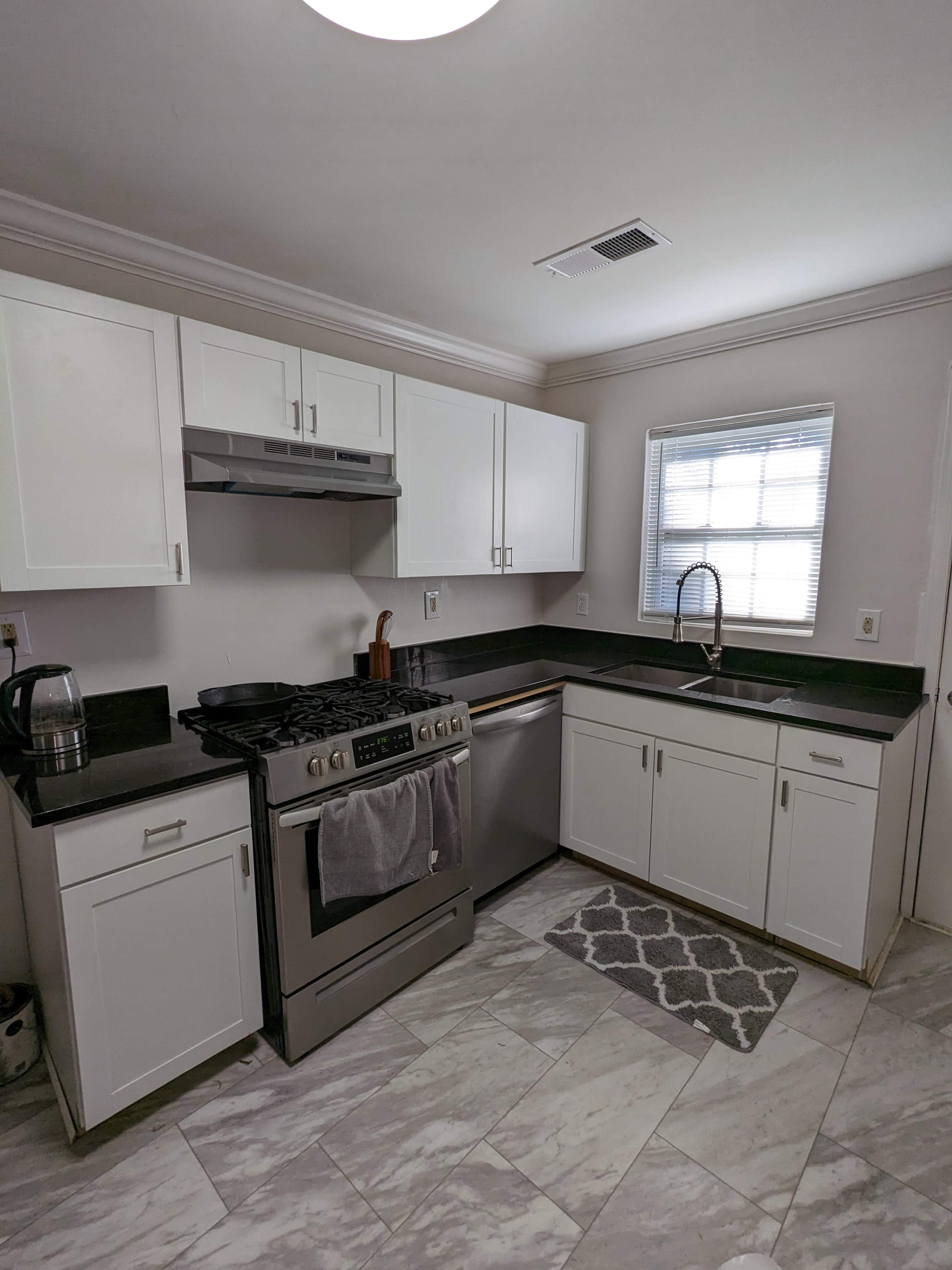 A modern kitchen features white cabinets, a stainless steel stove, a silver dishwasher, and a window above the sink.