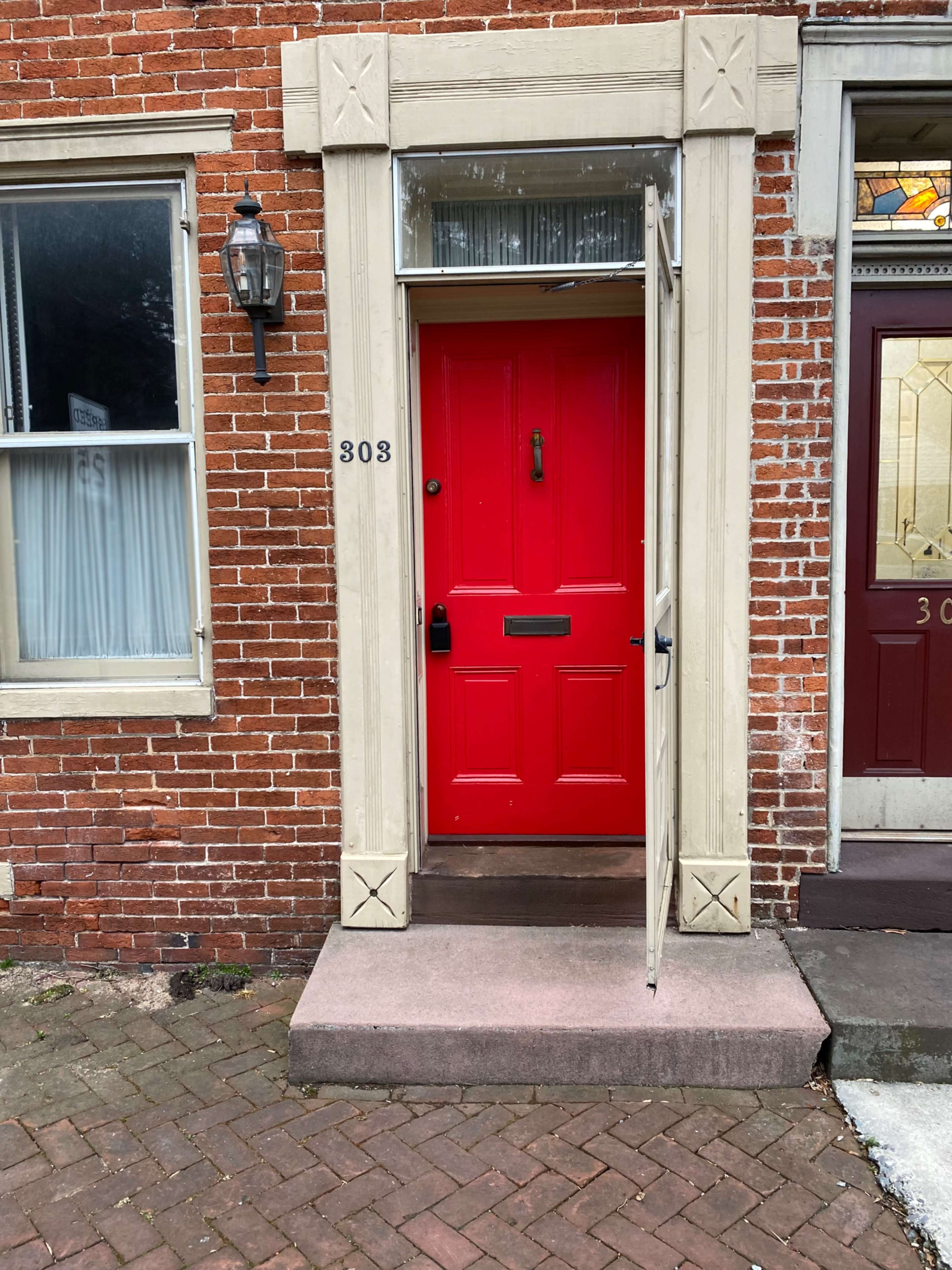 A red door framed by light-colored trim, set against a brick wall, with the number "308" displayed beside it.