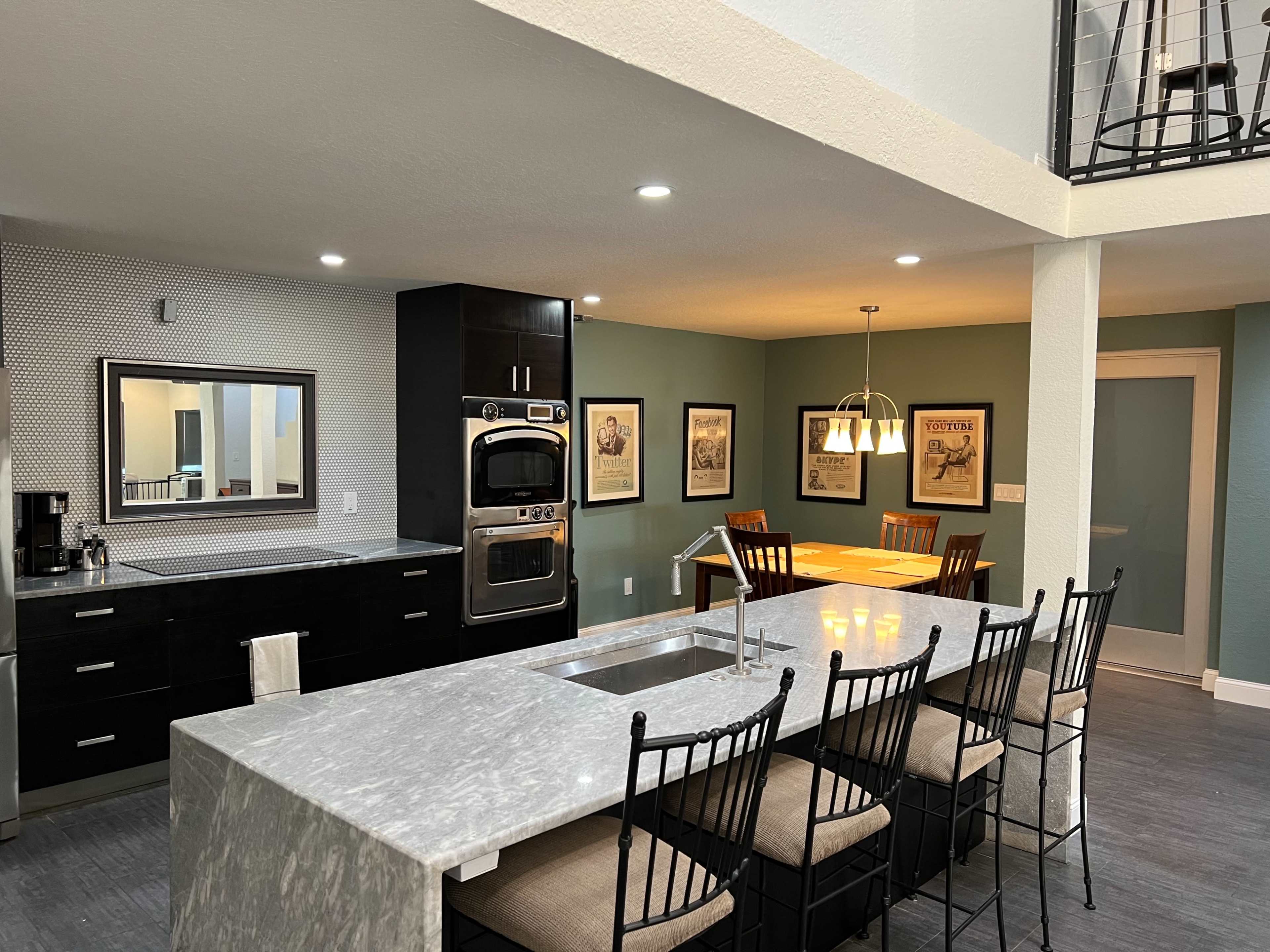 A modern kitchen and dining area with dark cabinets, a marble island, and a dining table with framed artwork on the walls.