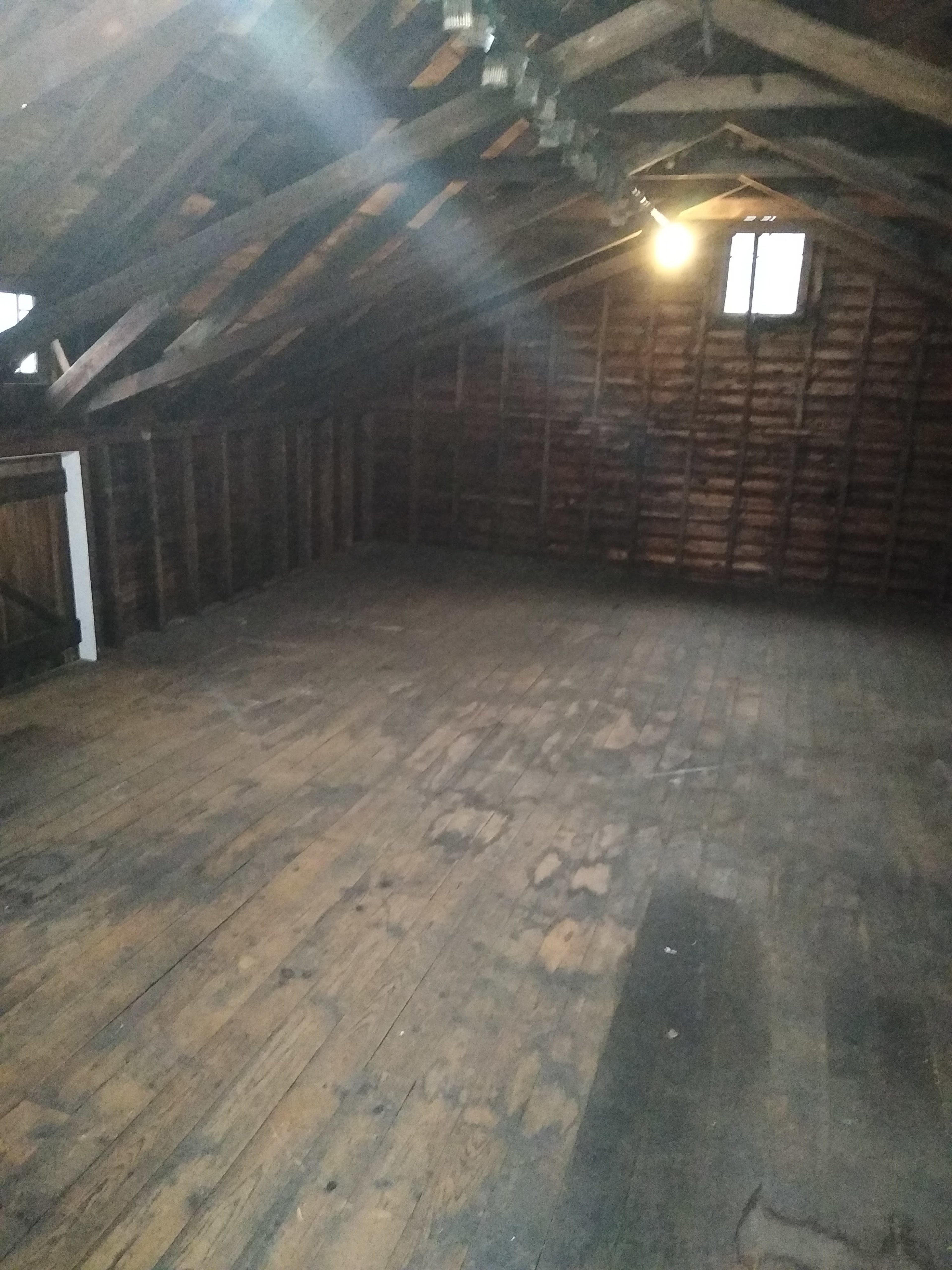 A spacious, empty attic with wooden beams and a floor made of planks.