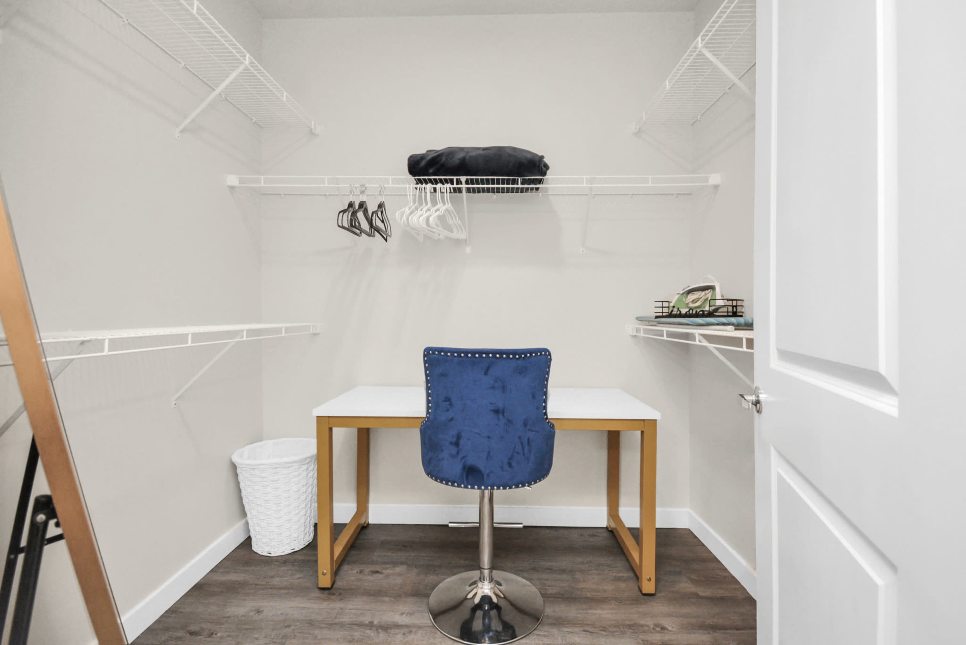 The image shows a small, organized closet with a desk and blue chair, along with shelving and a laundry basket.