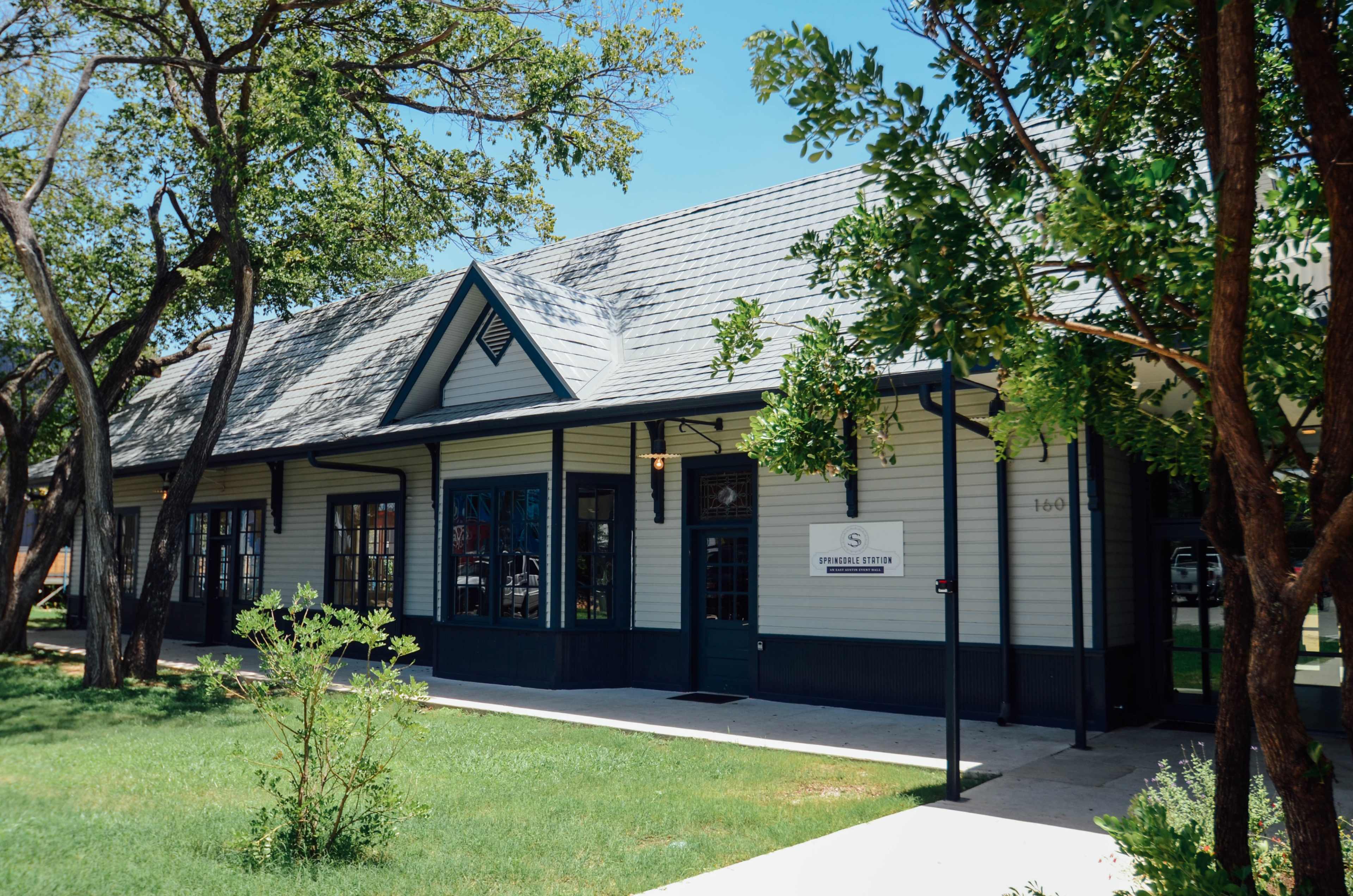 A single-story building with a peaked roof, large windows, and a well-maintained lawn surrounded by trees.