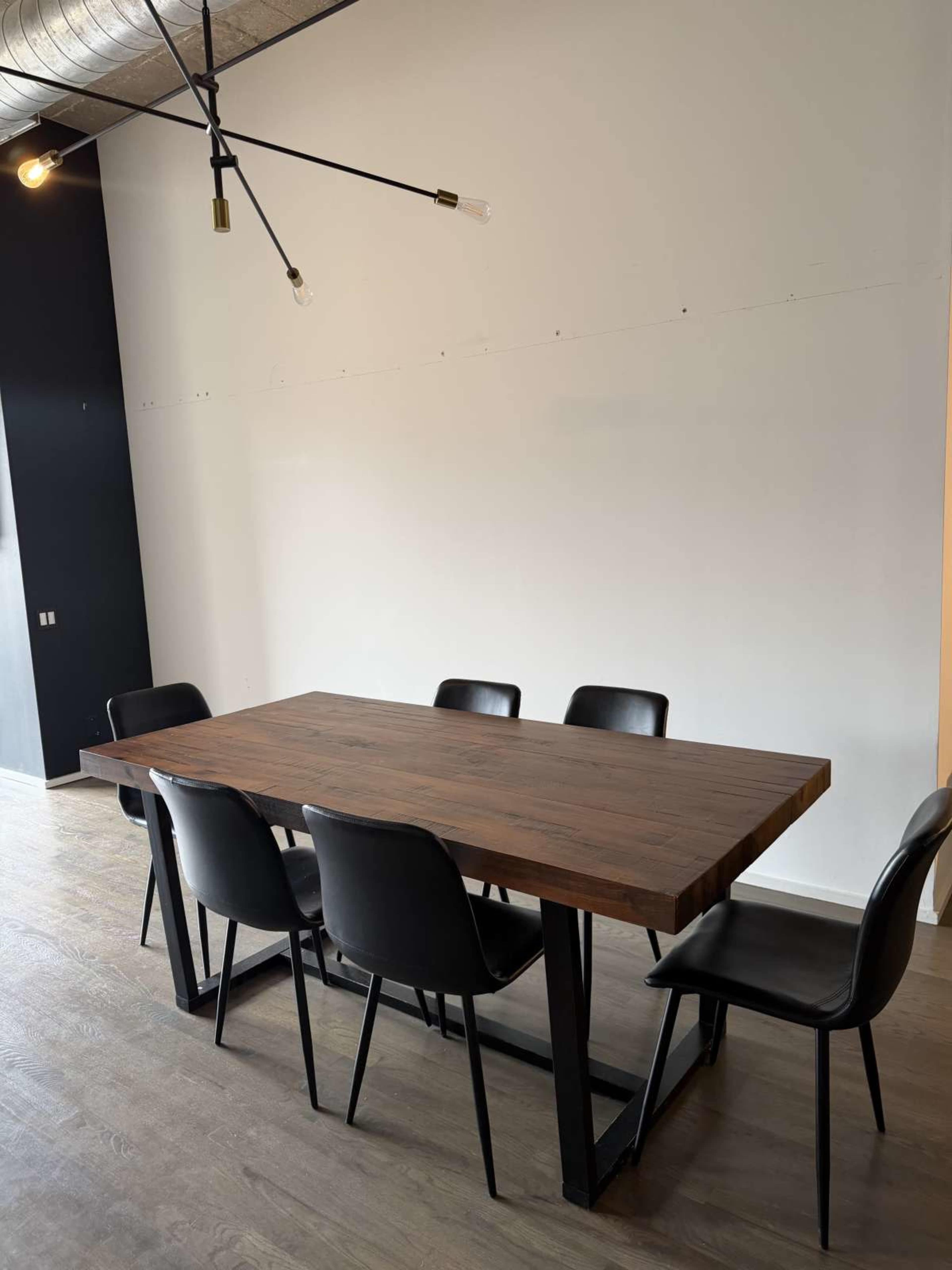 A wooden dining table with a metal base is surrounded by six black chairs in a minimalist room.