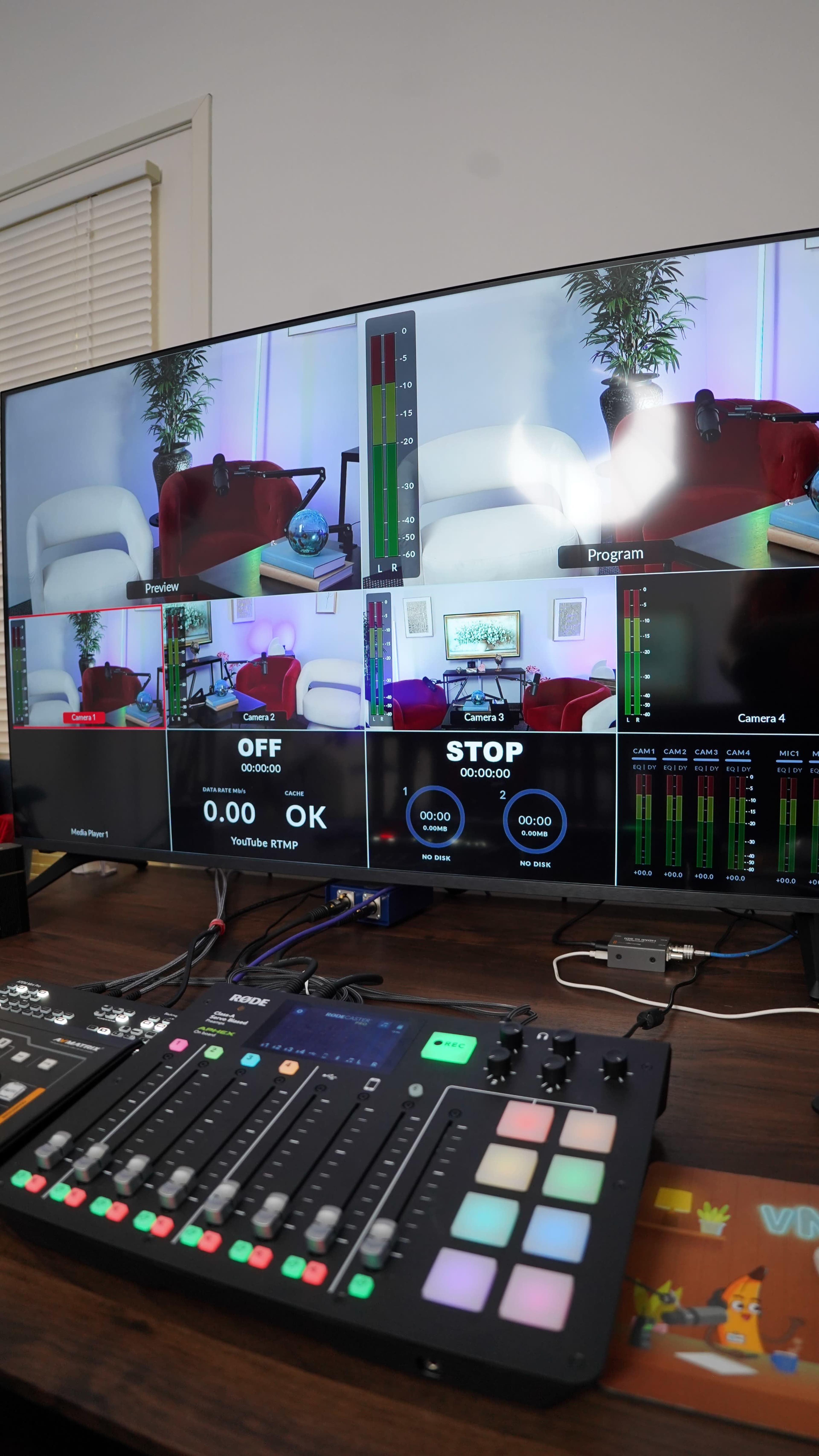 The image displays a large monitor showing multiple camera feeds and a control panel with various buttons and indicators, set up for a live streaming broadcast.