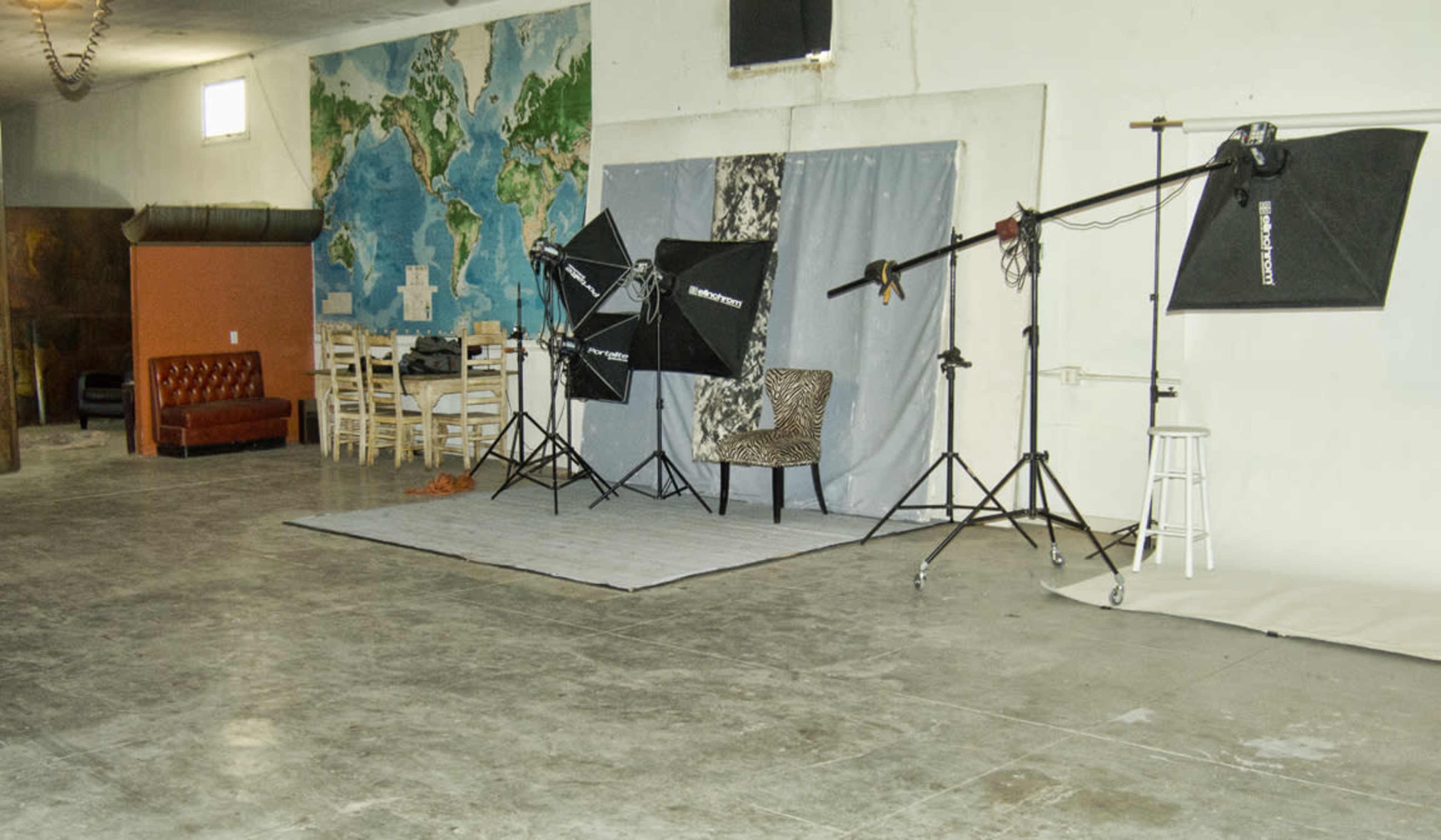 A spacious studio with a world map mural, photography lighting equipment, a patterned chair, and a wooden dining table with chairs.