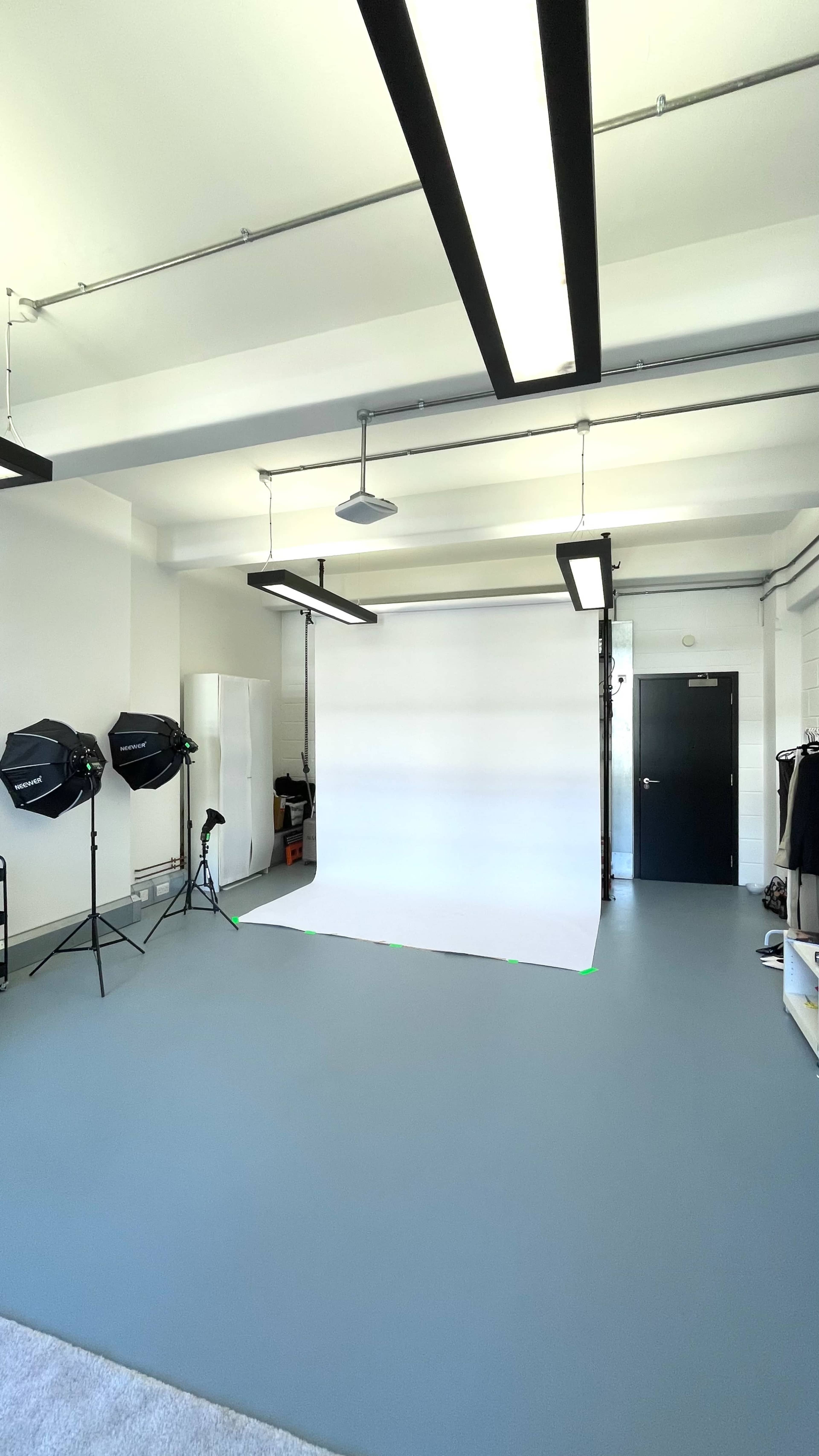 The image shows a photography studio with a plain white backdrop, lighting equipment, and a neatly organized space.