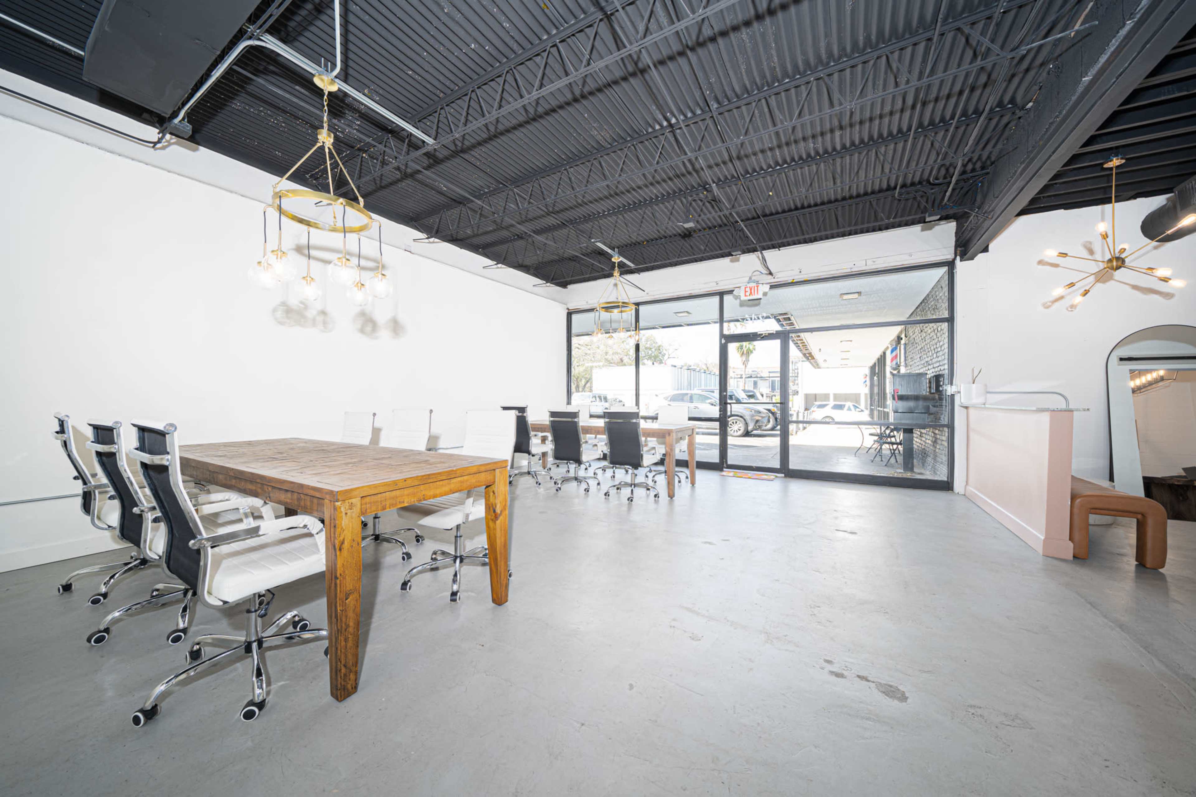 The image shows an open office space with a large table and white office chairs on one side, and a glass door leading to an exterior area on the other side.
