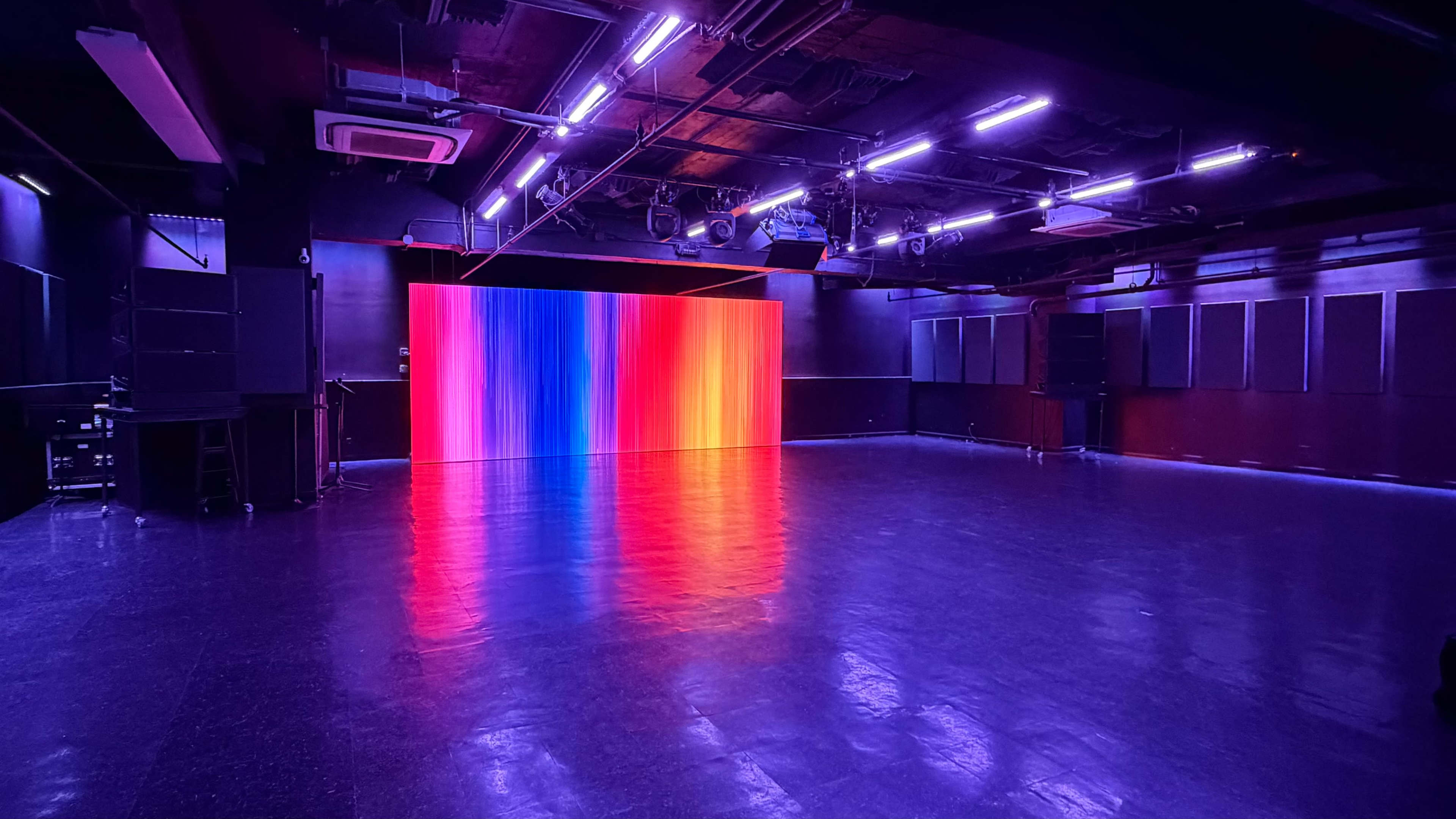 The image shows a spacious dance studio with polished black flooring and a brightly lit, colorful backdrop in the center.