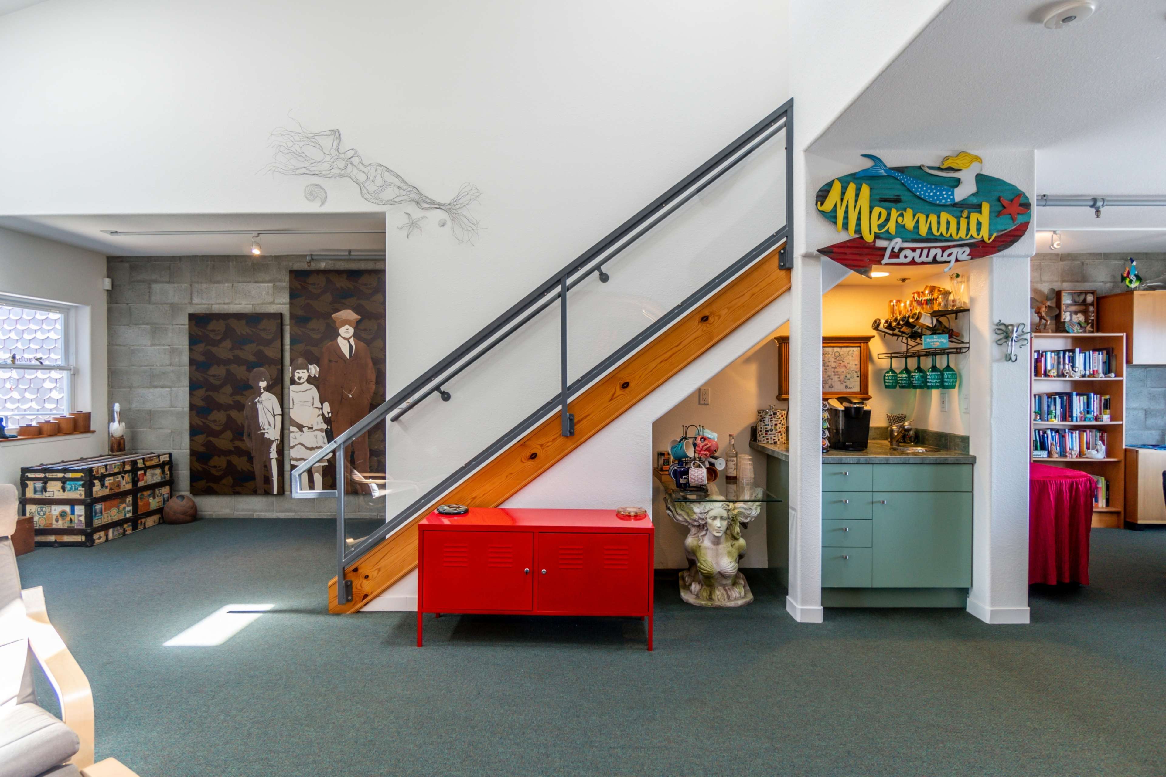 The image shows a brightly lit interior space featuring a staircase on the left, a red cabinet, and a decorated wall labeled "Mermaid Lounge."