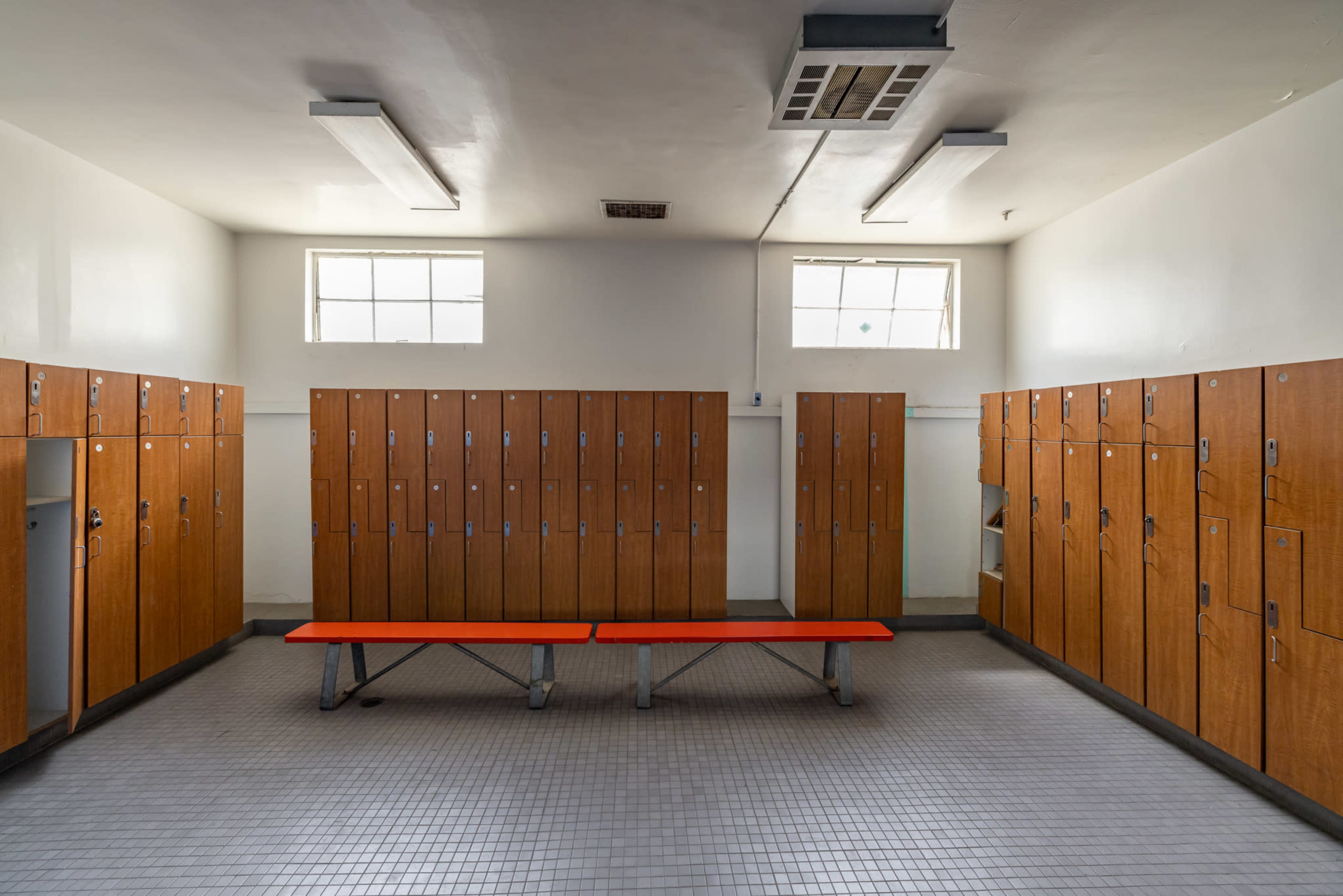 A clean locker room with wooden lockers lining the walls and a red bench in the center.