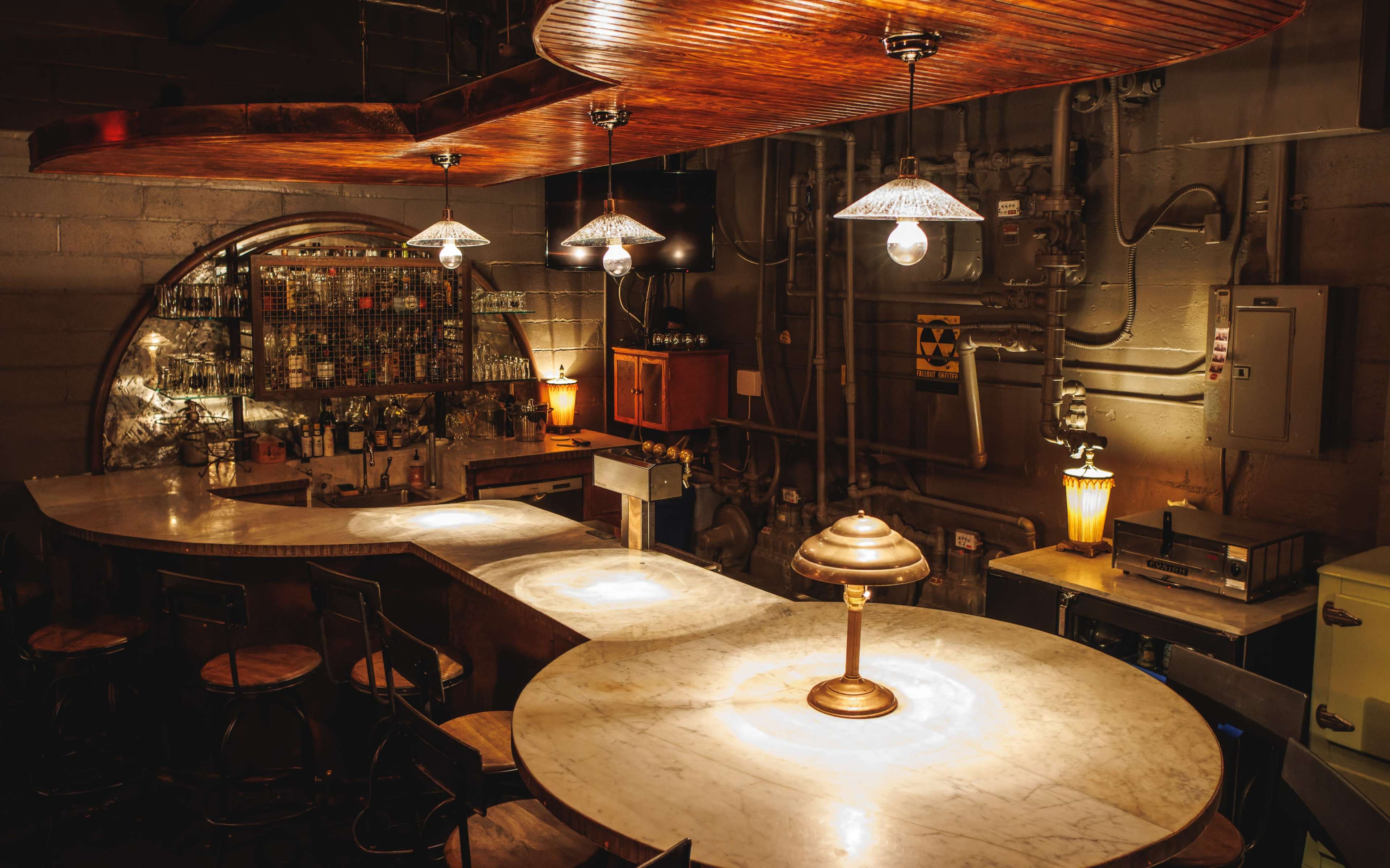 A dimly lit bar features a white marble countertop, wooden accents, and vintage lamps hanging above.