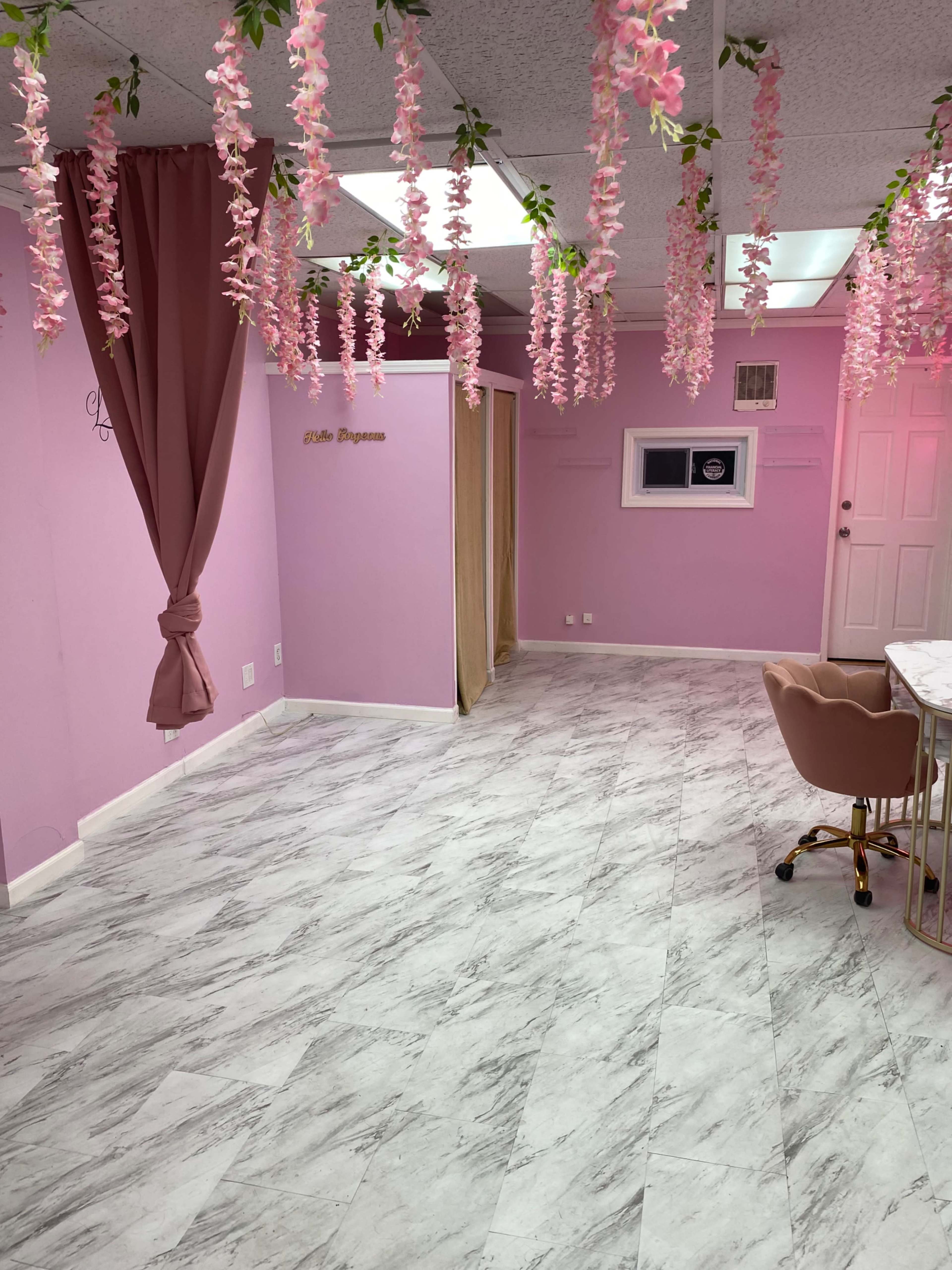 A softly lit interior of a room with pink walls, floral decorations hanging from the ceiling, and a marble-patterned floor.