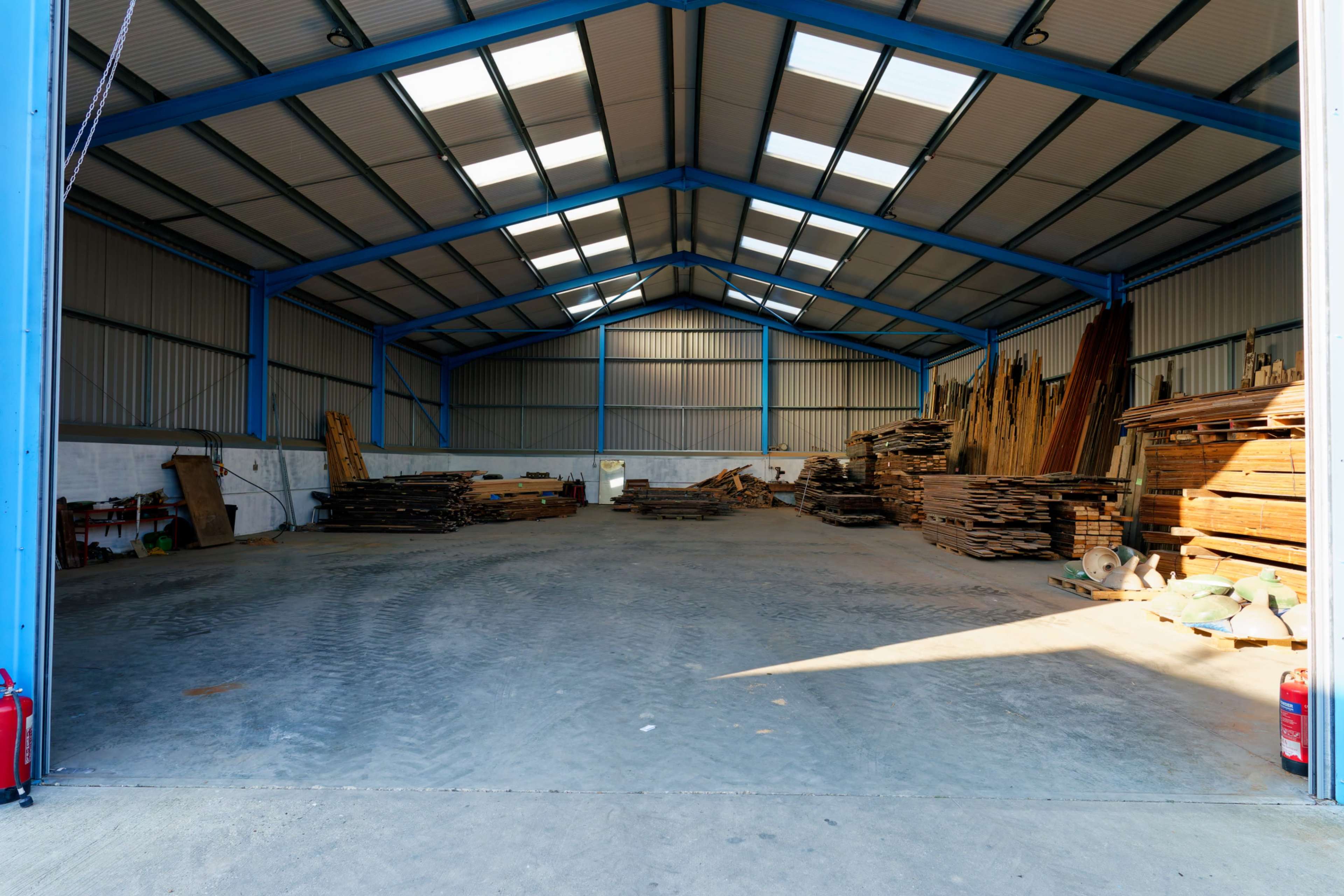 The image shows the interior of a spacious warehouse with stacked wooden planks and beams against the walls.