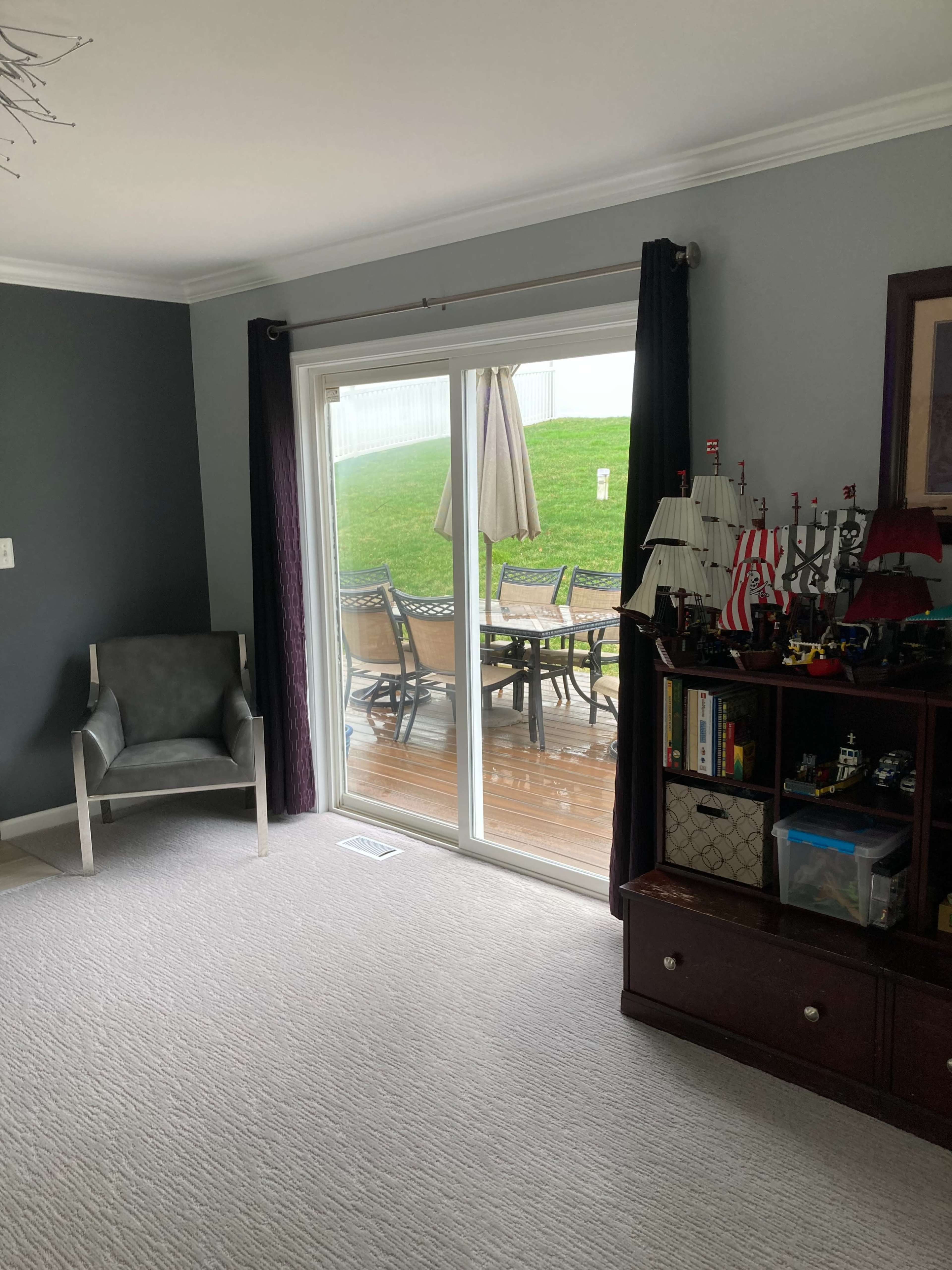 A living room with a gray wall, a chair, and a view of a patio through sliding glass doors.
