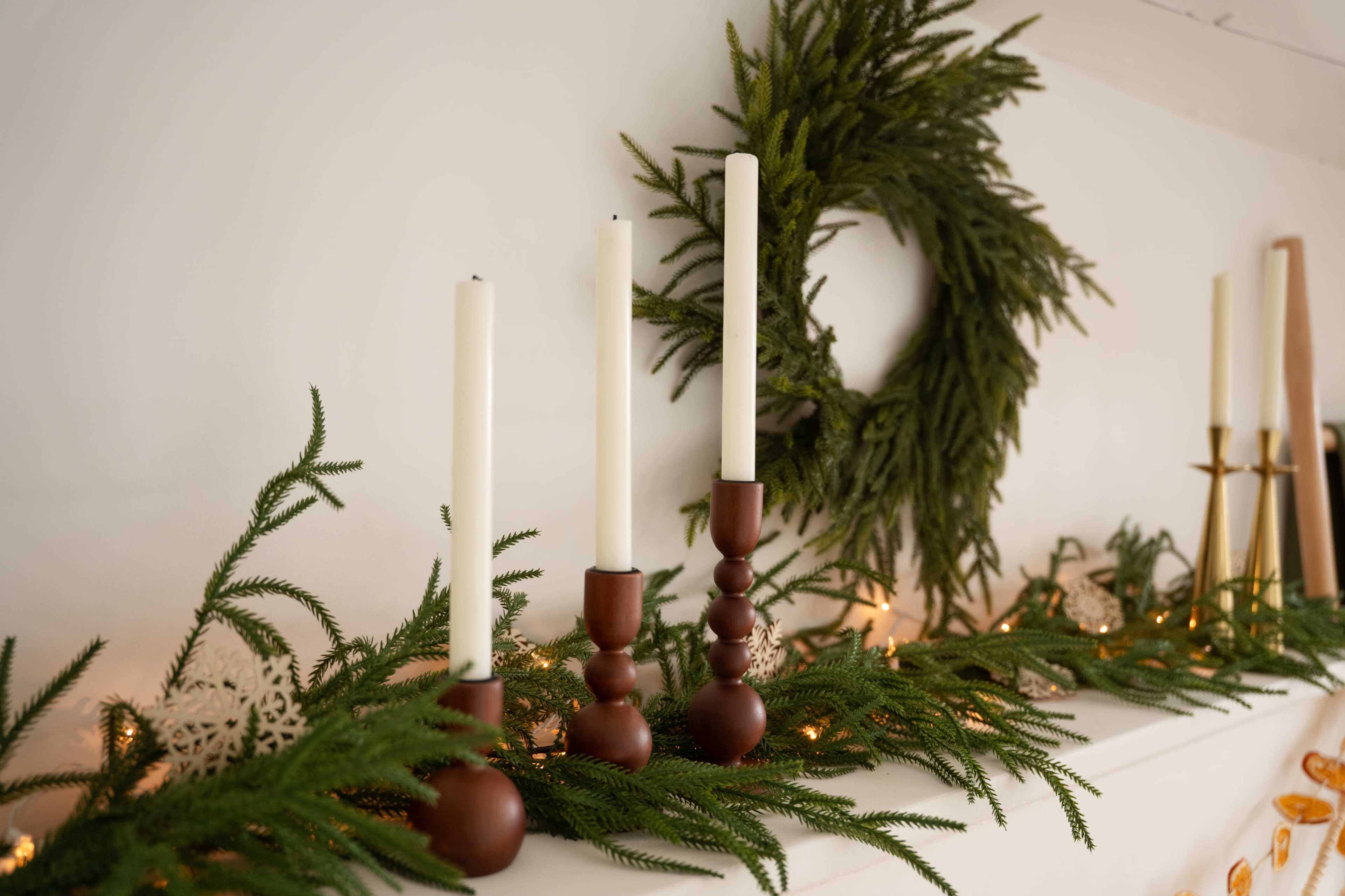 The image shows three candles placed on a decorative mantle adorned with greenery and a wreath in the background.