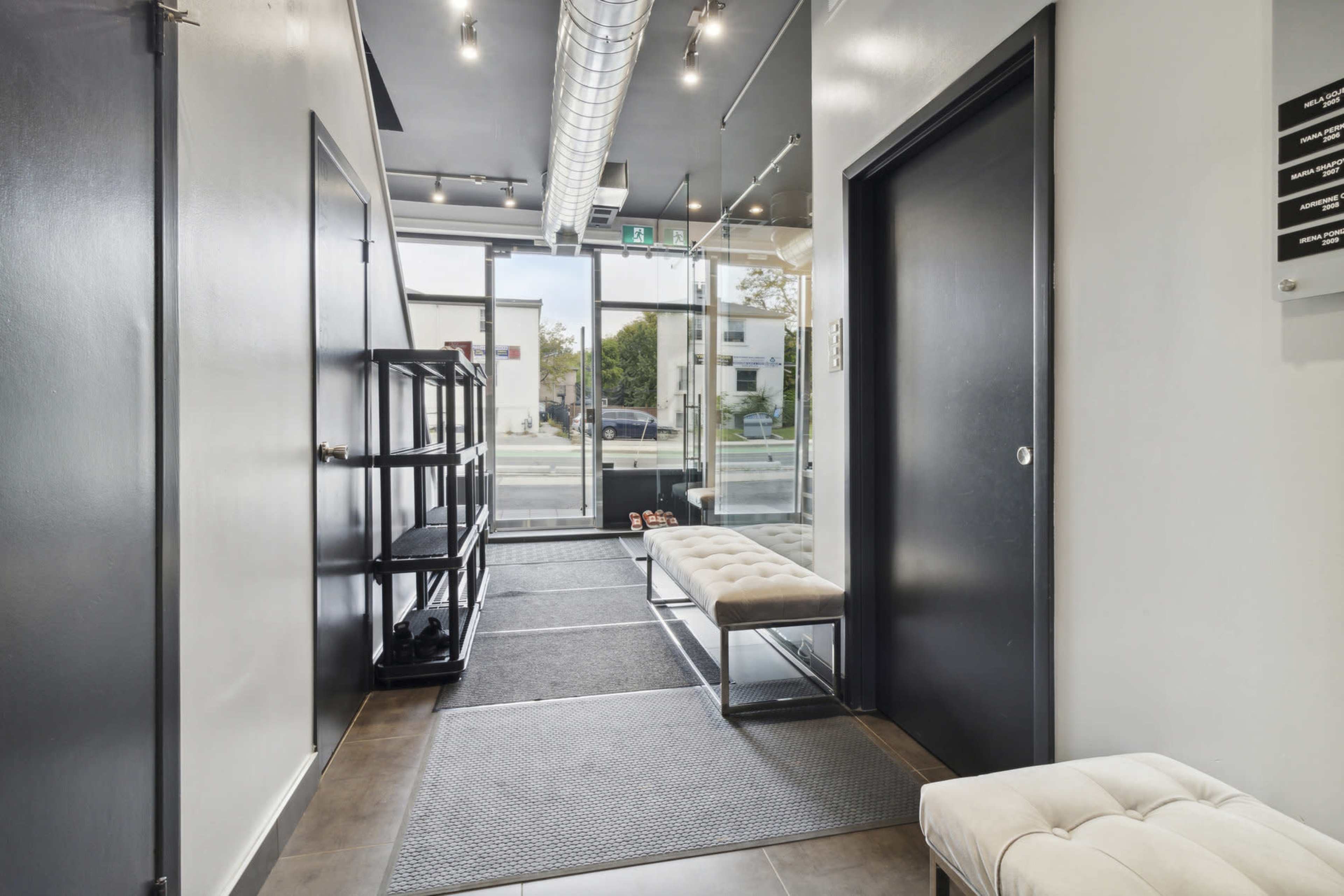 The image shows a modern hallway featuring a bench, a shelf, and large glass doors leading to the exterior.