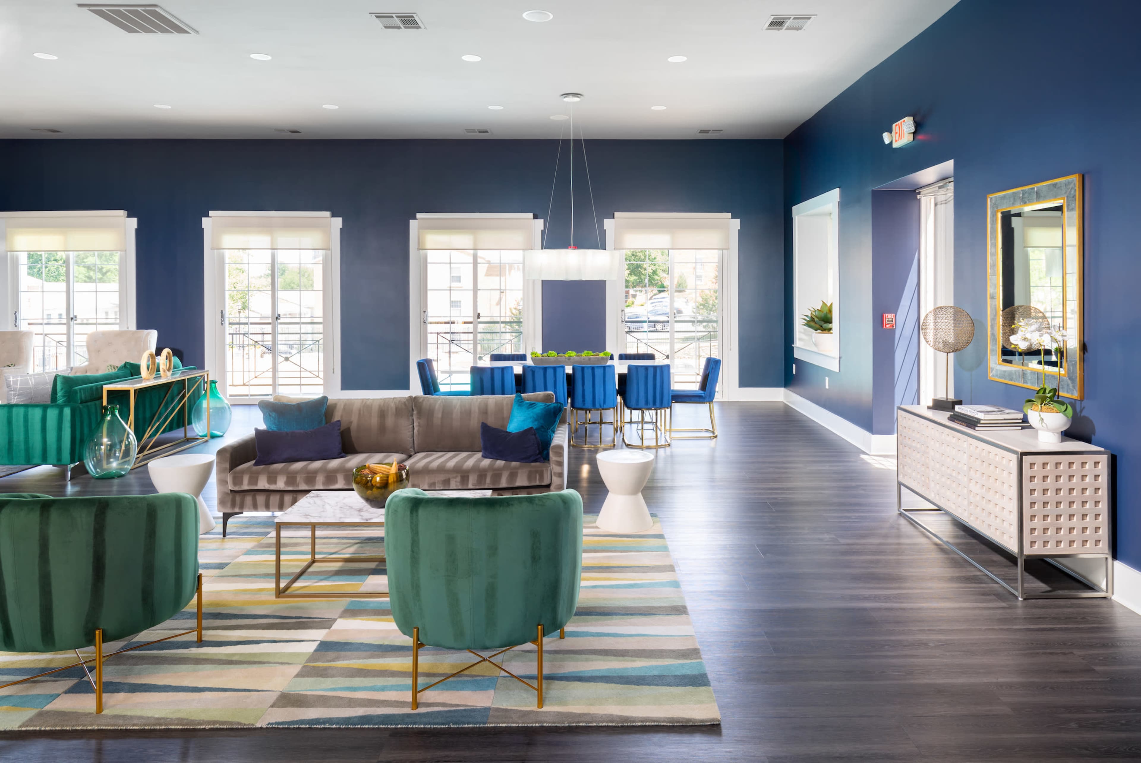 A modern living space featuring a seating area with green chairs, a gray sofa, a patterned rug, and a dining area with blue chairs against a dark blue wall.